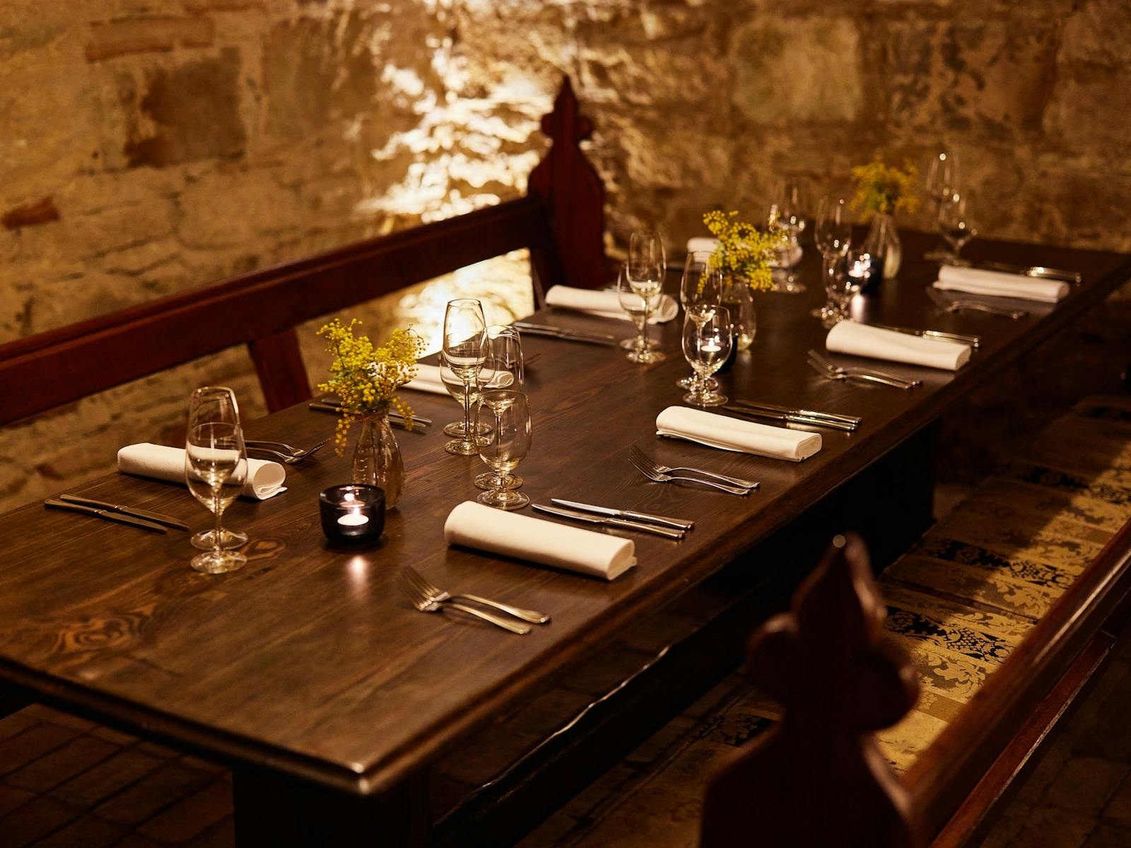 Cellar dining table set for 8 people, dimly lit with candlelight and limestone walls.