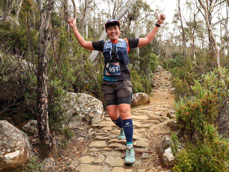 A female runner on the Organ Pipes Track with arms in the arm and a large smile