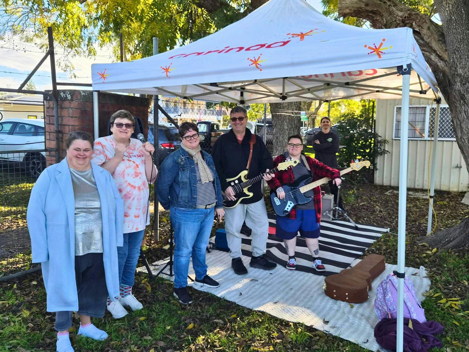 Members of the Hi Abilities Live group pose beneath a white Caringa Australia marquee at an outdoor