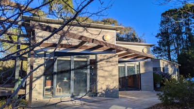 A small grey concrete building with a brown pergola structure out the front. Clear blue skies.