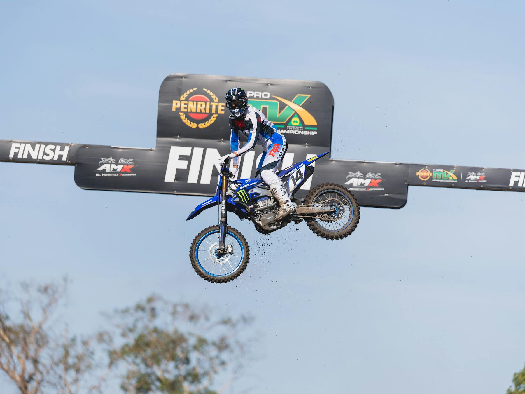 A motocross rider triumphantly celebrates in the air crossing the finish line