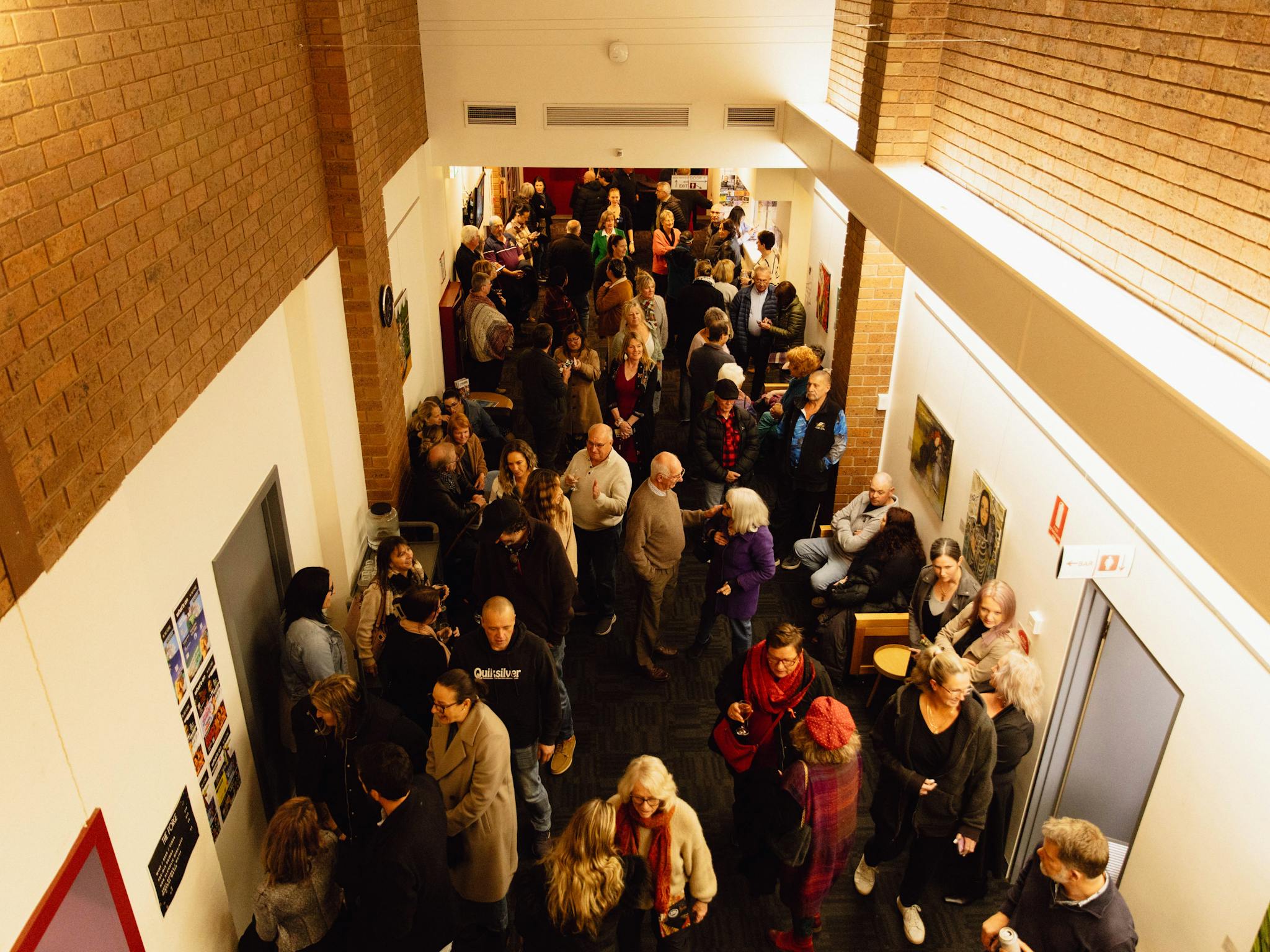 Lots of people are gathered together in a narrow passage way which is the foyer of the venue