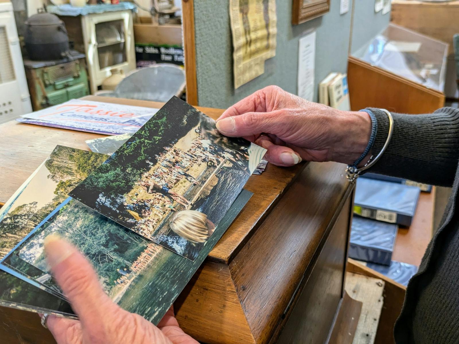 Hands, holding historic photographs at the Derby Schoolhouse Museum, surrounded by artifacts.