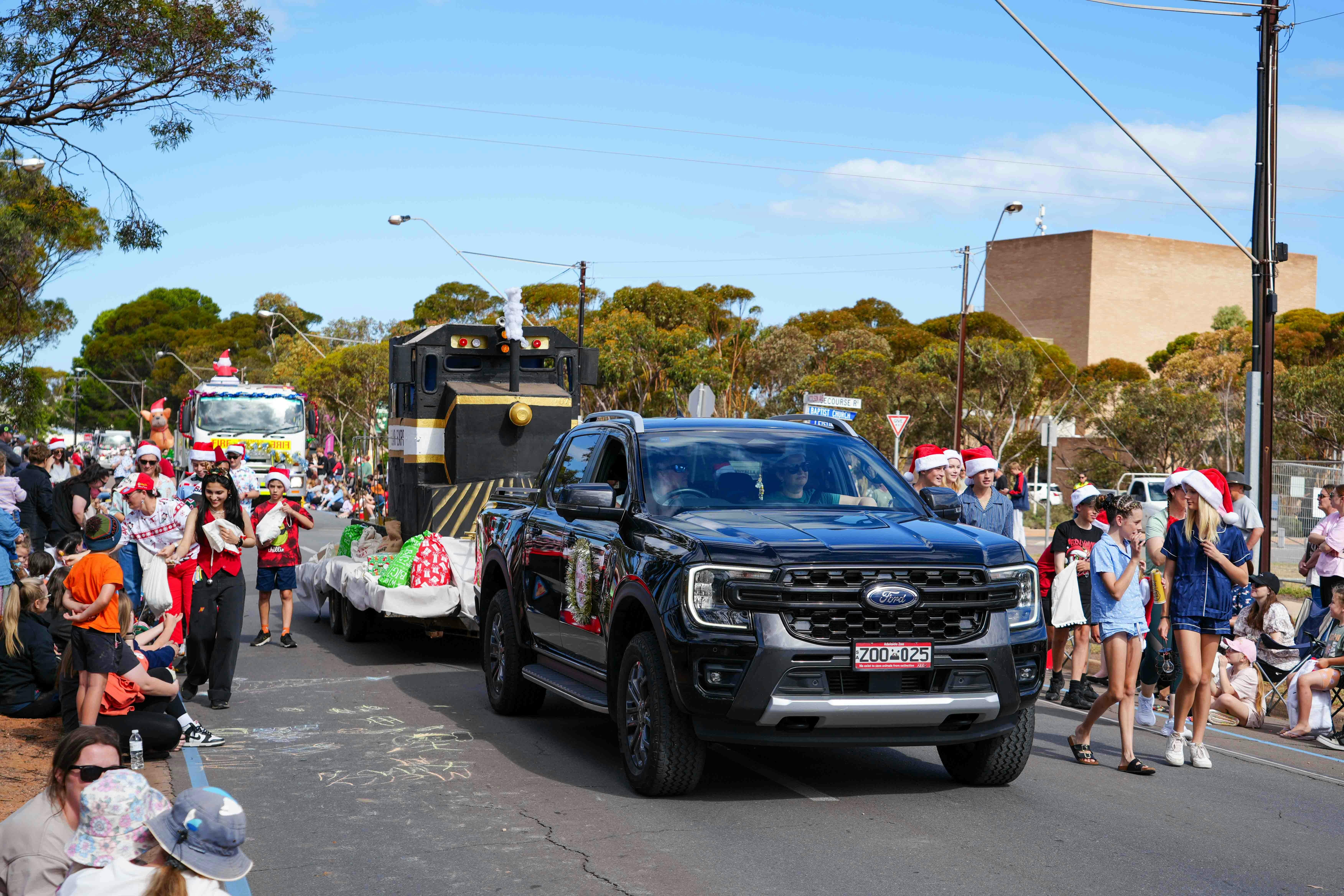 A black ute tows a Polar Express train float with people dressed up walking alongside