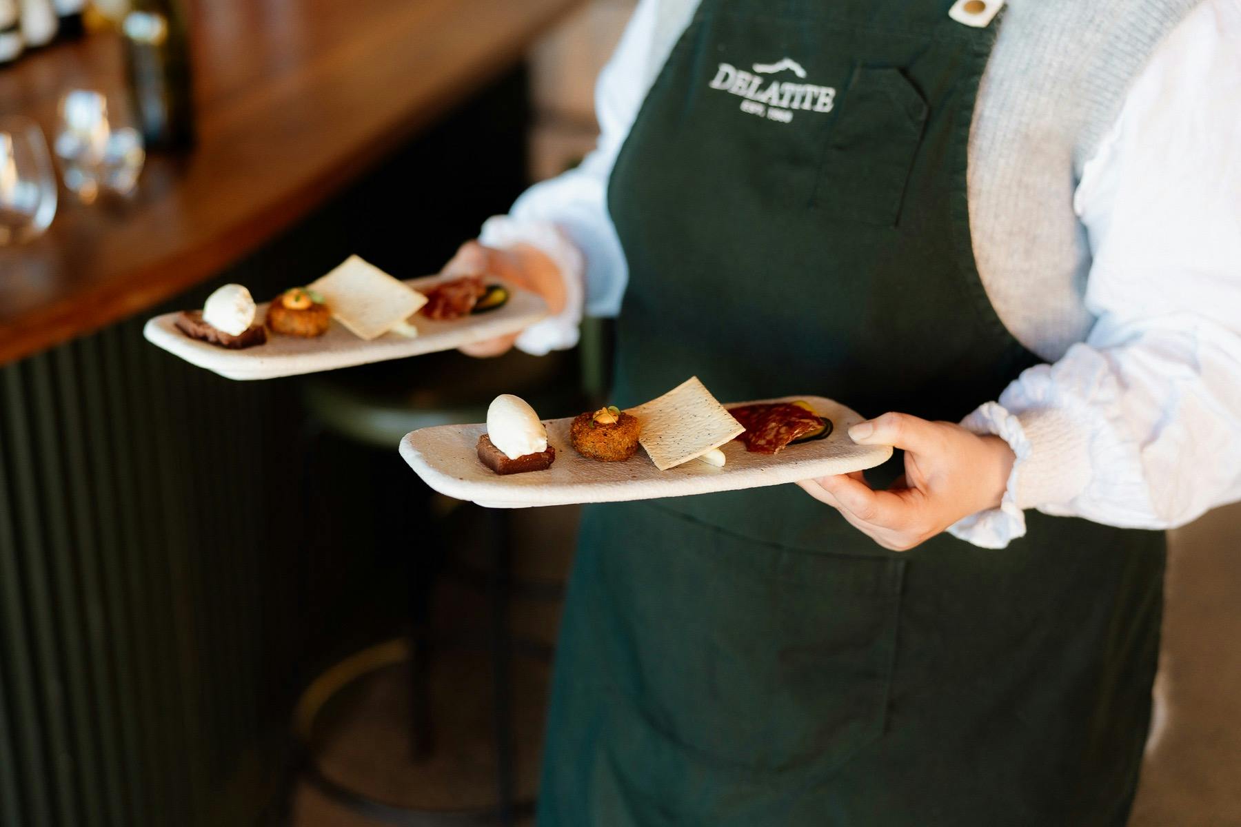 someone holding two plates with four mini degustation morsels on each plate