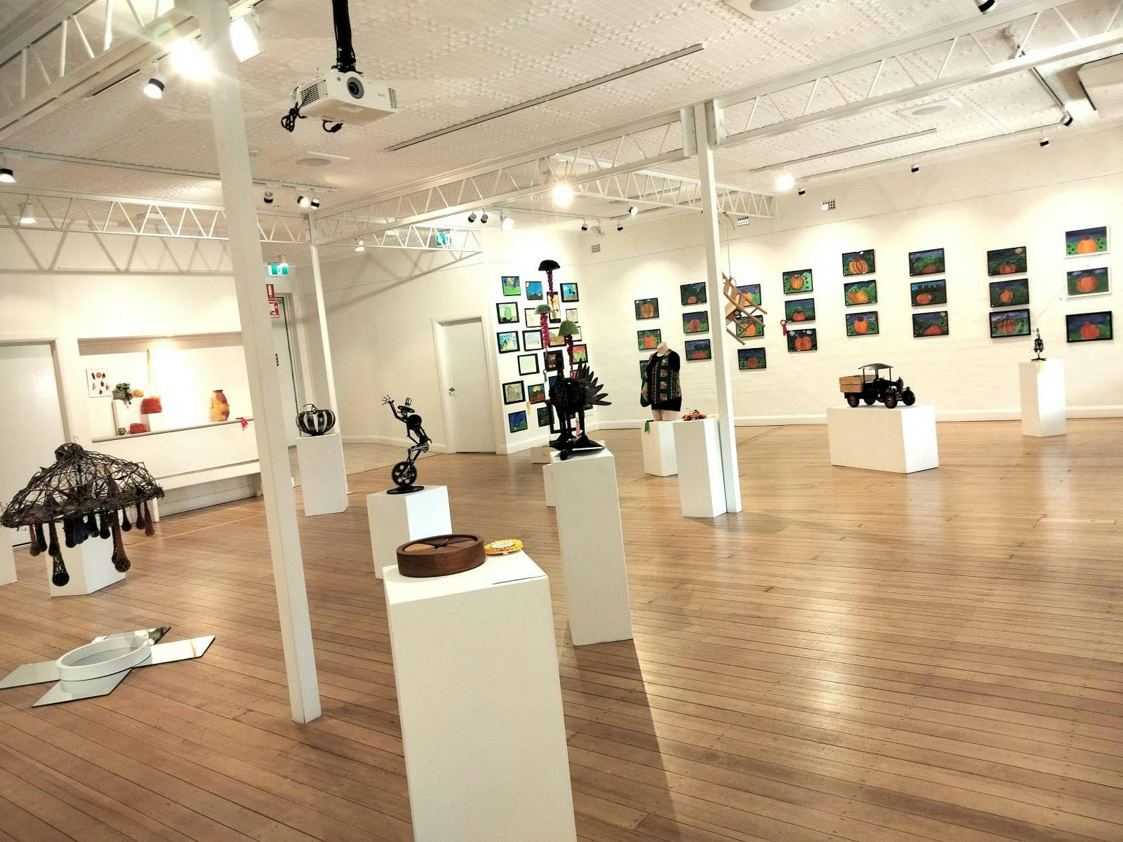 A room full of varied craftwork on plinths and paintings on walls.