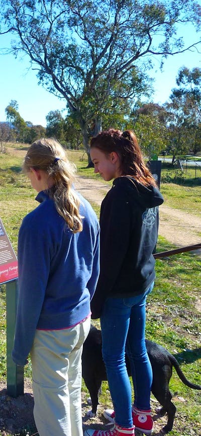 Two girls with dog at a sign board in open woodland
