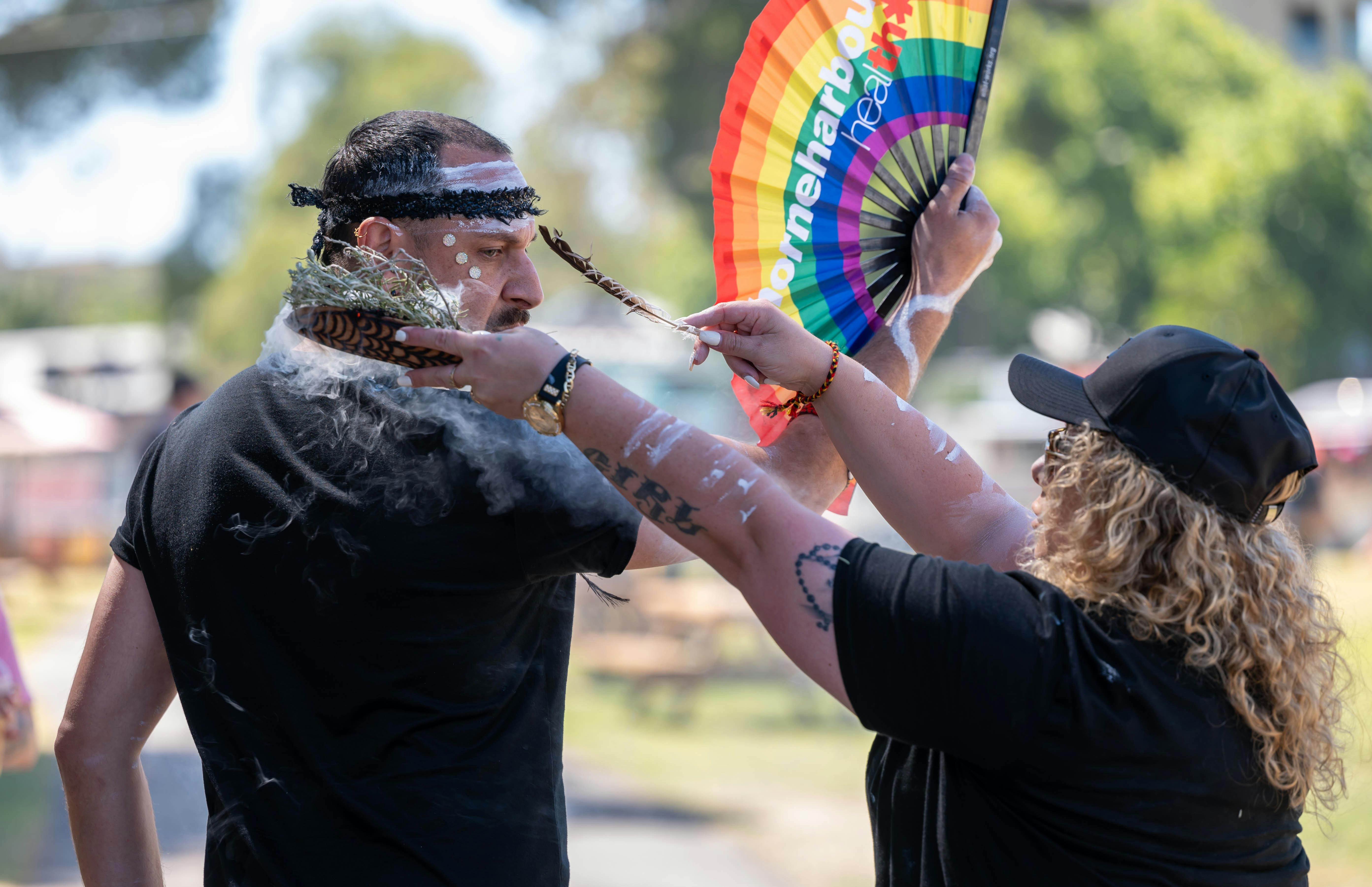 A person is being smudged with smoke, holding a rainbow fan.