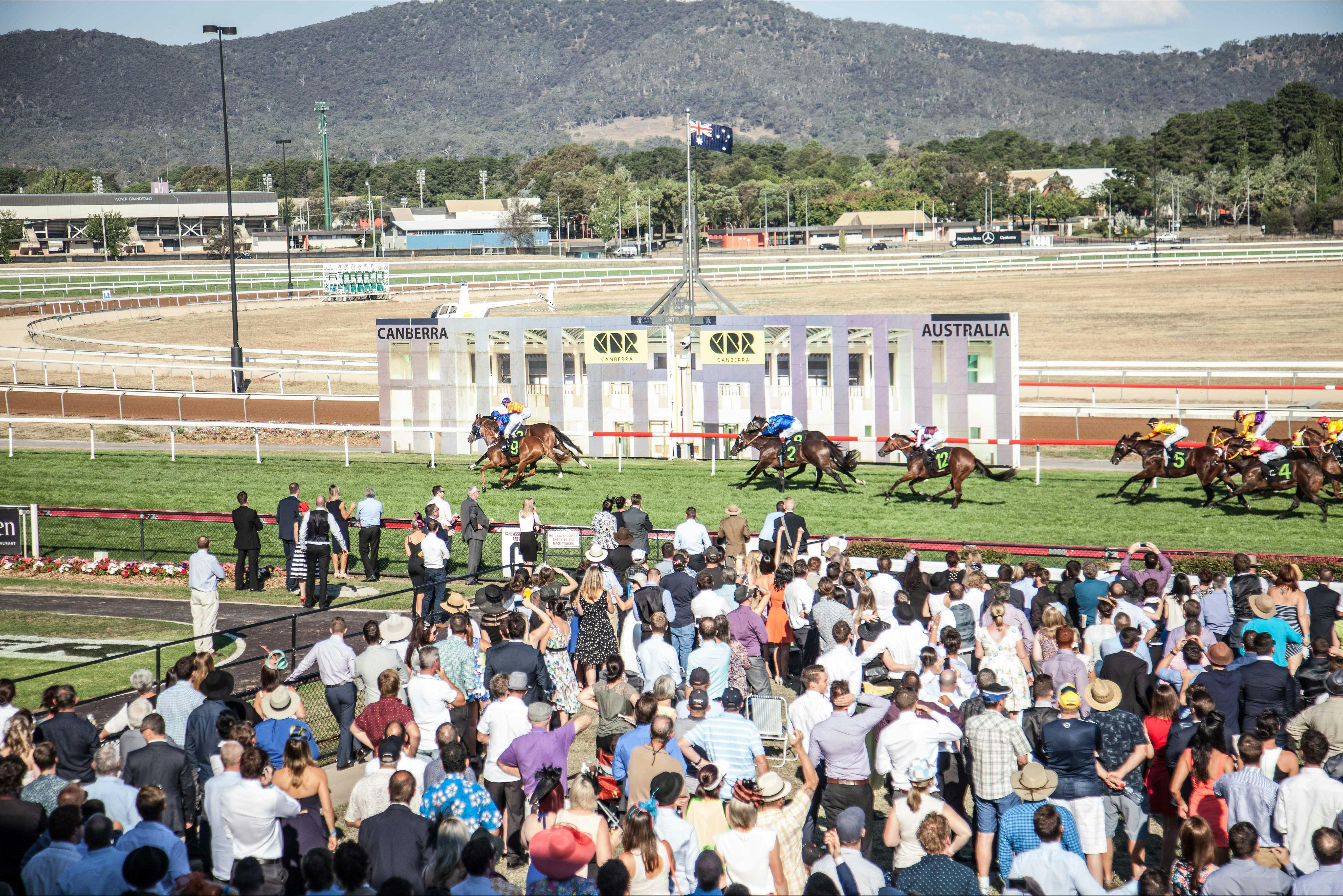 View of horses crossing the finishing post in front of a crowded stand
