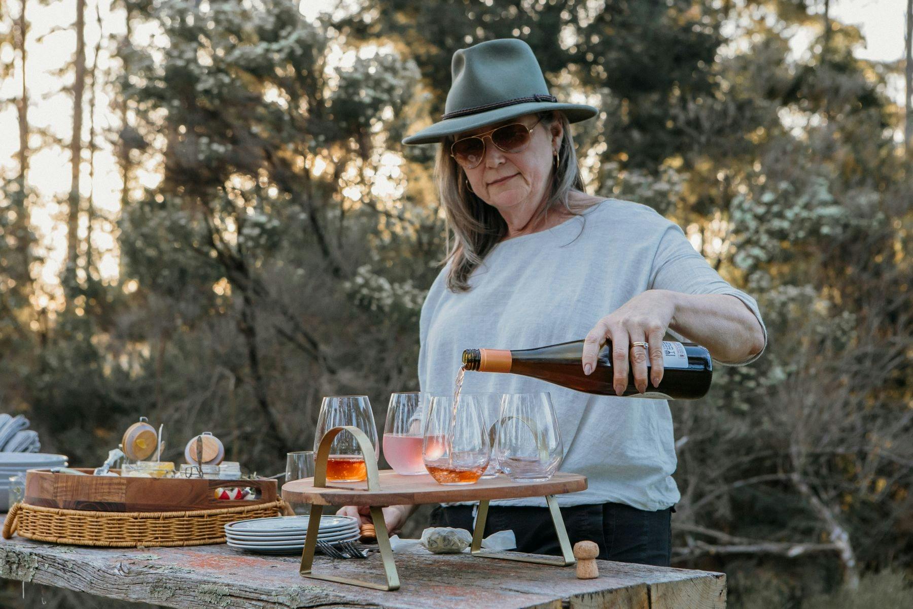 Woman standing in bush camp setting pouring wine into glasses