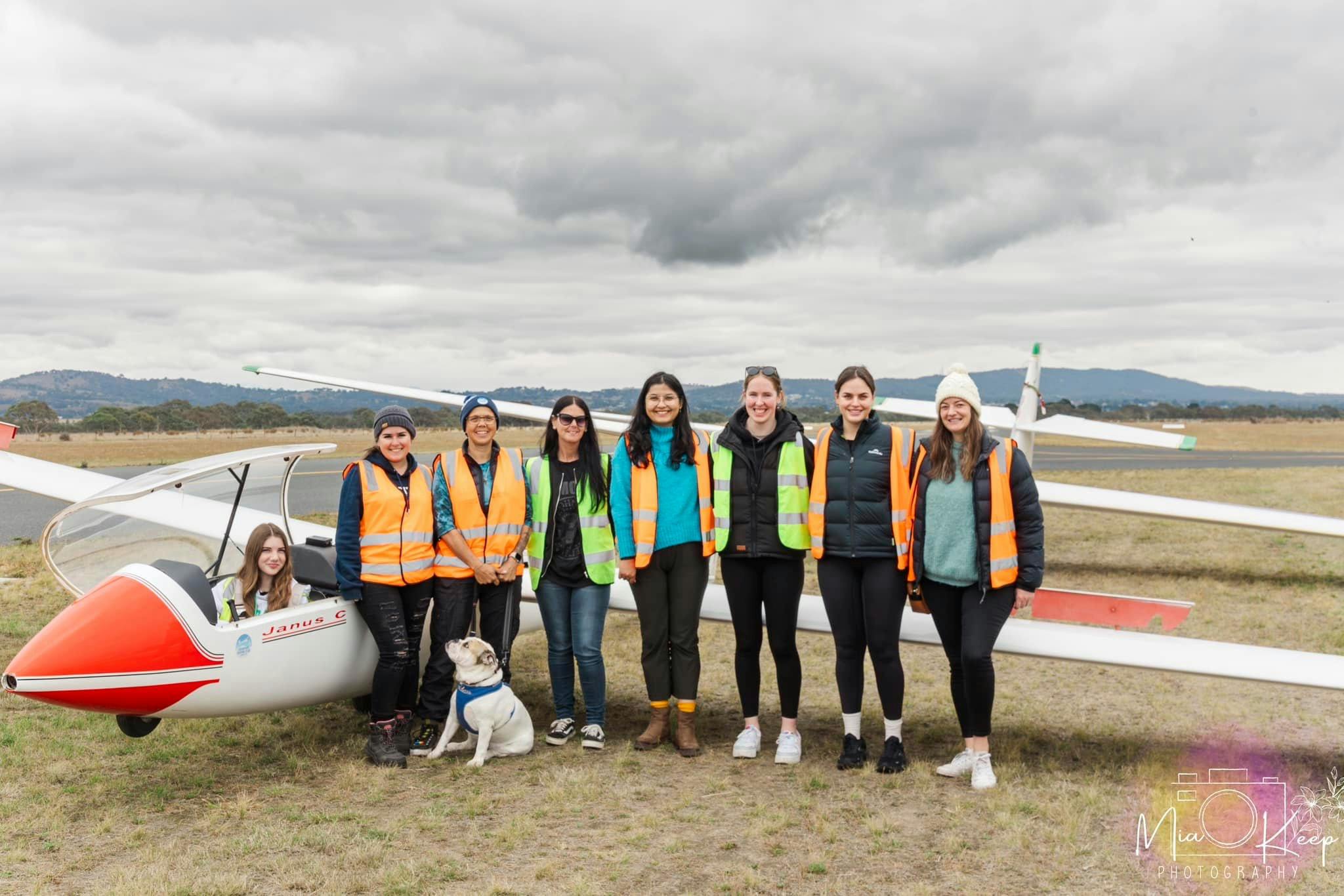 Eight people and a dog standing in front of a plane on a runway