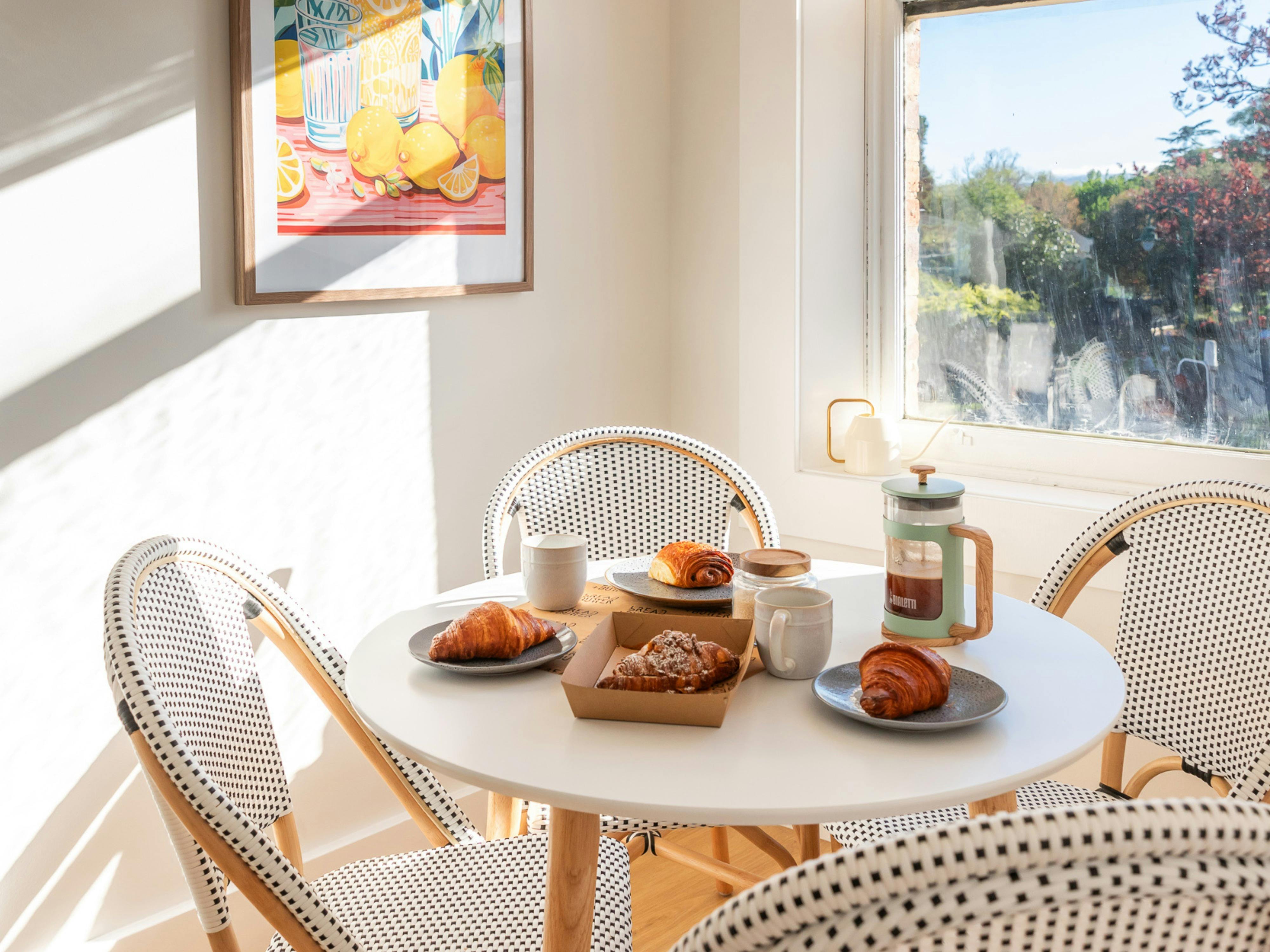 round white dining table, black and white chairs, coffee plunger and pastries set on table