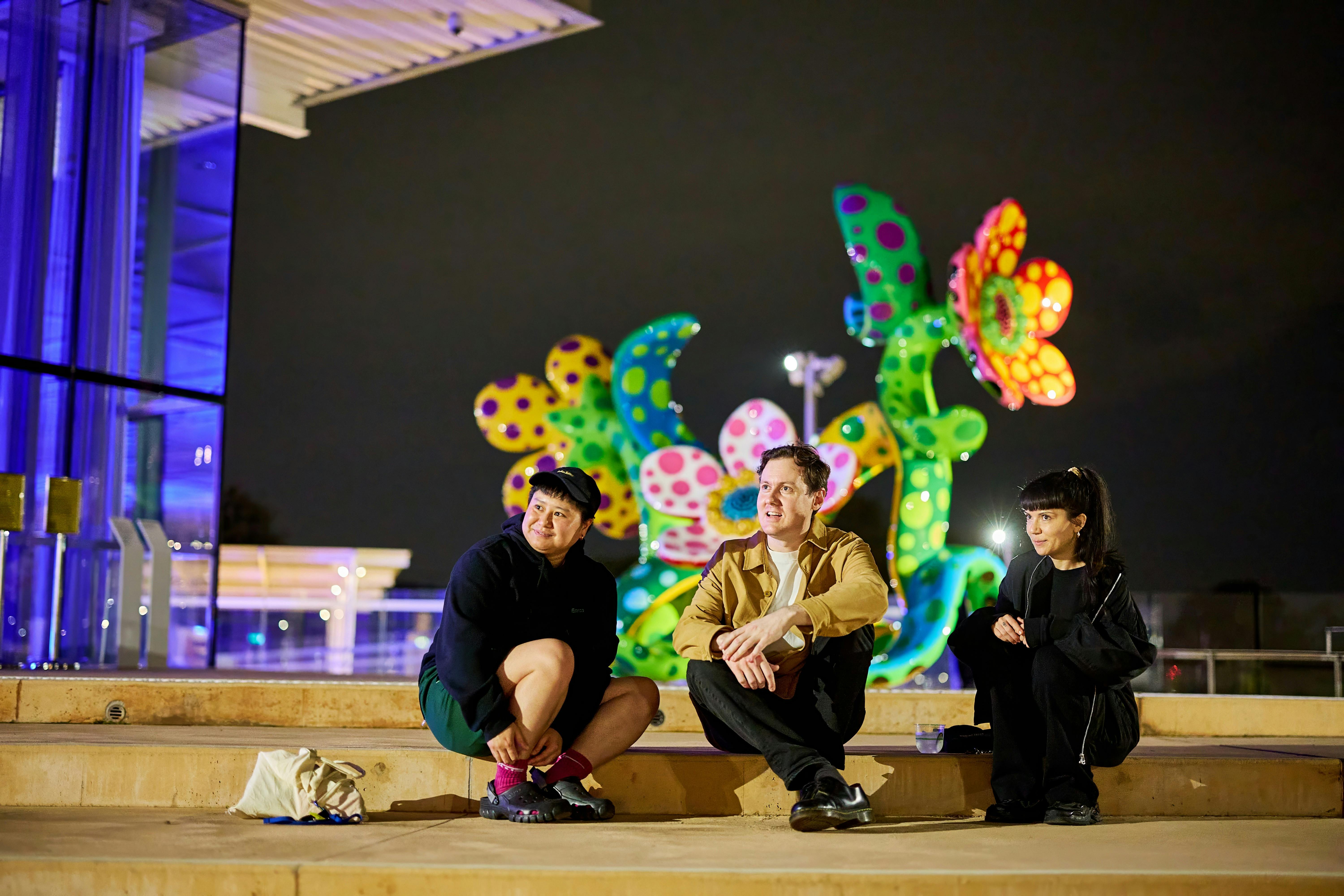 Three people seated outside on the terrace beside Flowers that Bloom in the Cosmos by Yayoi Kusama