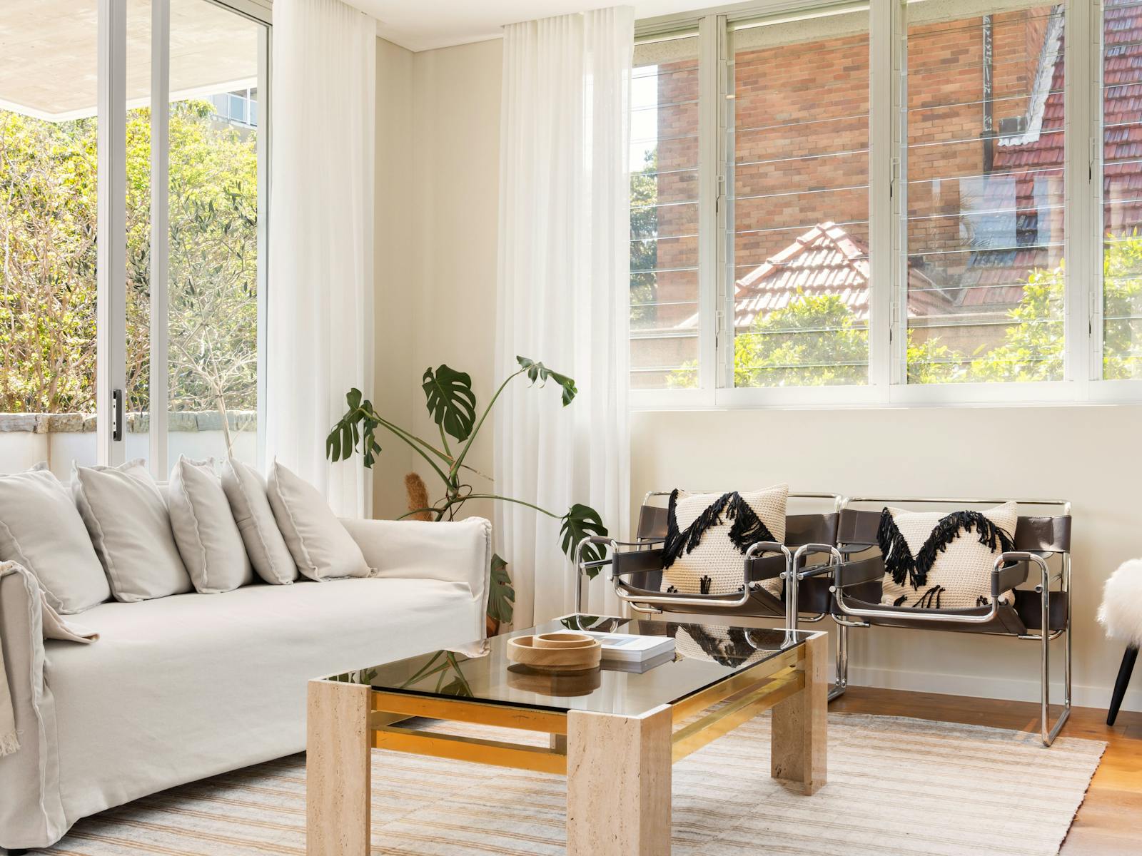 Living room with stylish chairs, a sofa, and large windows bringing in sunlight.