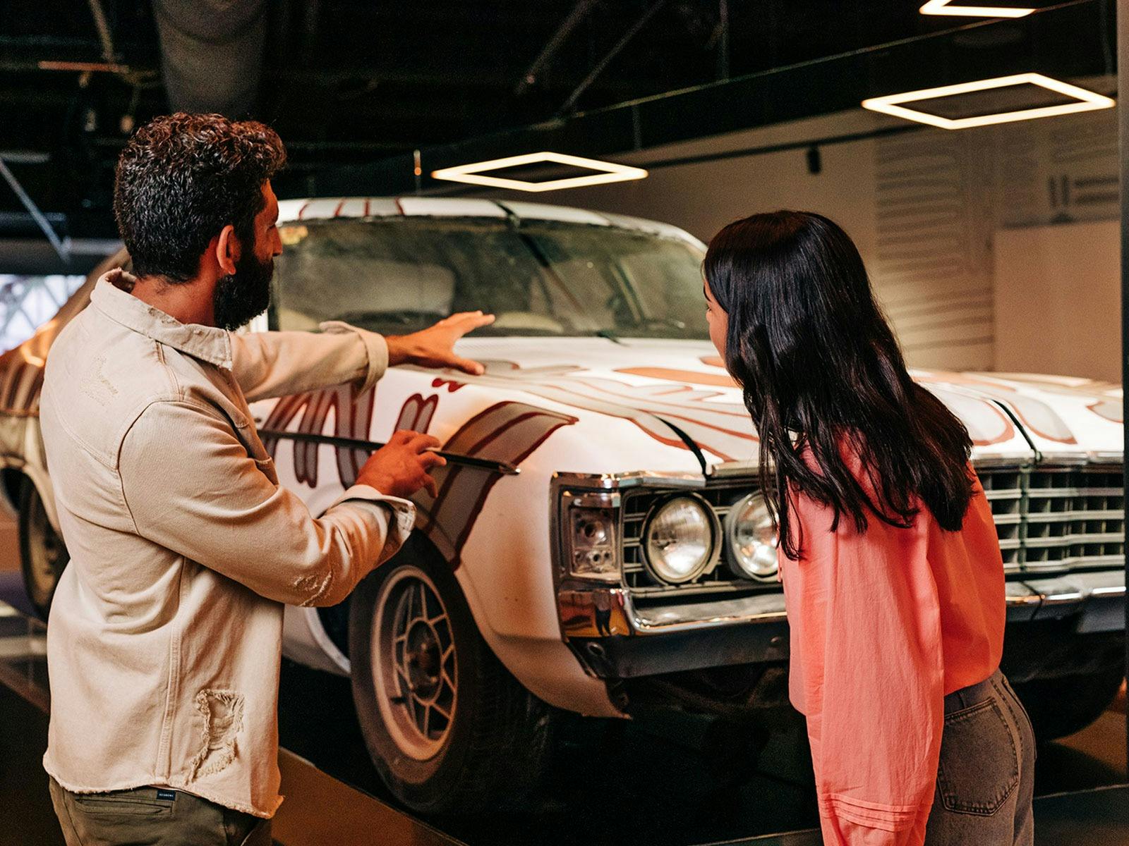 A man gestures at a car, as a young woman looks on