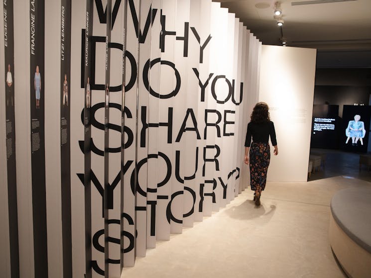 Person walking past a wall which reads "Why do you share your story?"