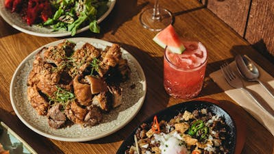 A wooden table filled with Filipino dishes including sizzling sisig with egg, crispy pork pieces, a