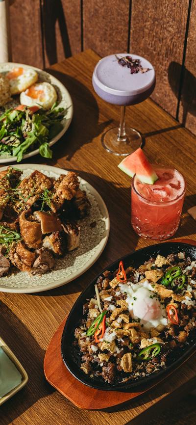 A wooden table filled with Filipino dishes including sizzling sisig with egg, crispy pork pieces, a