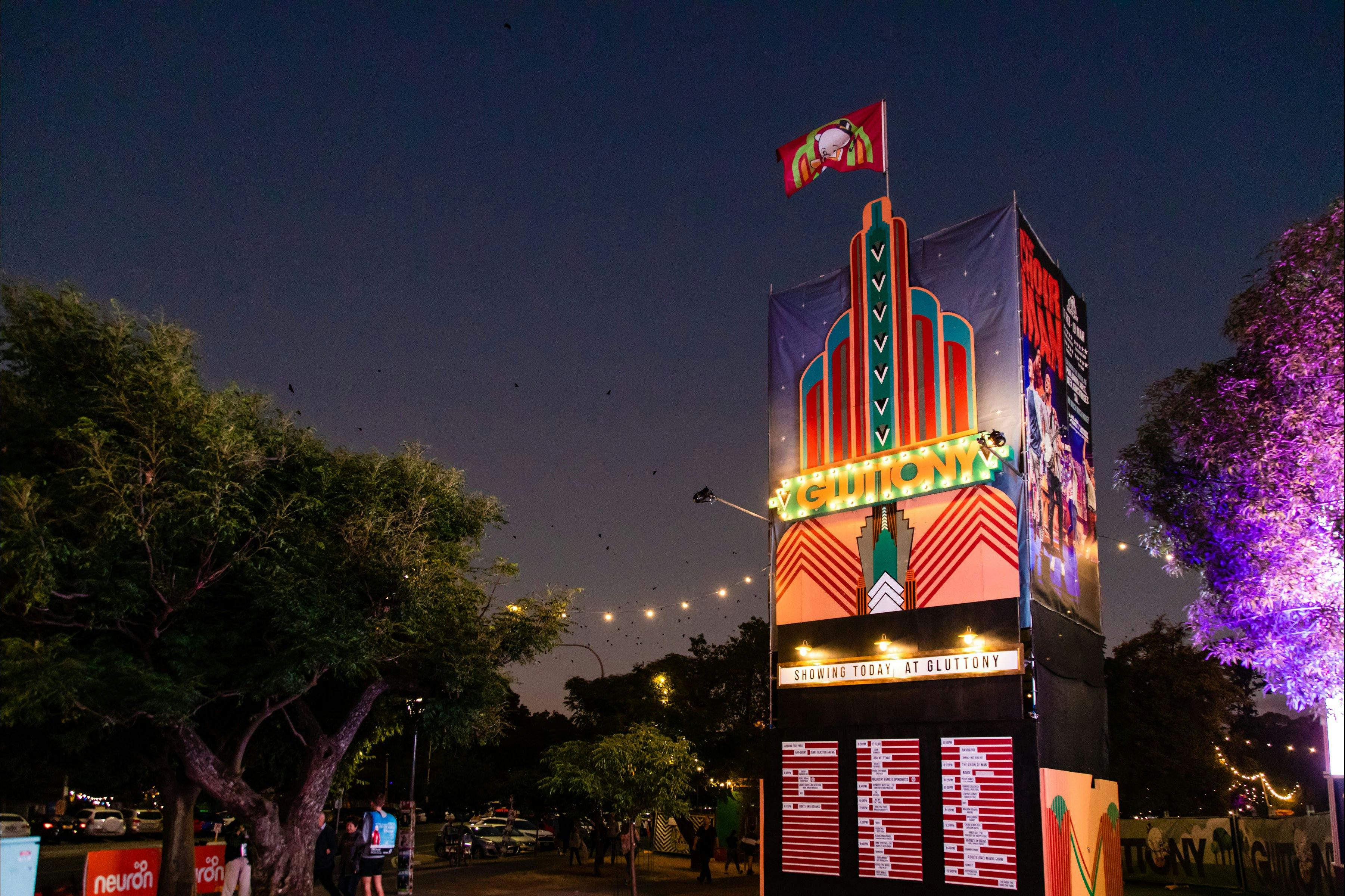 Gluttony Show Times Board lit up at night. Gluttony flag waving