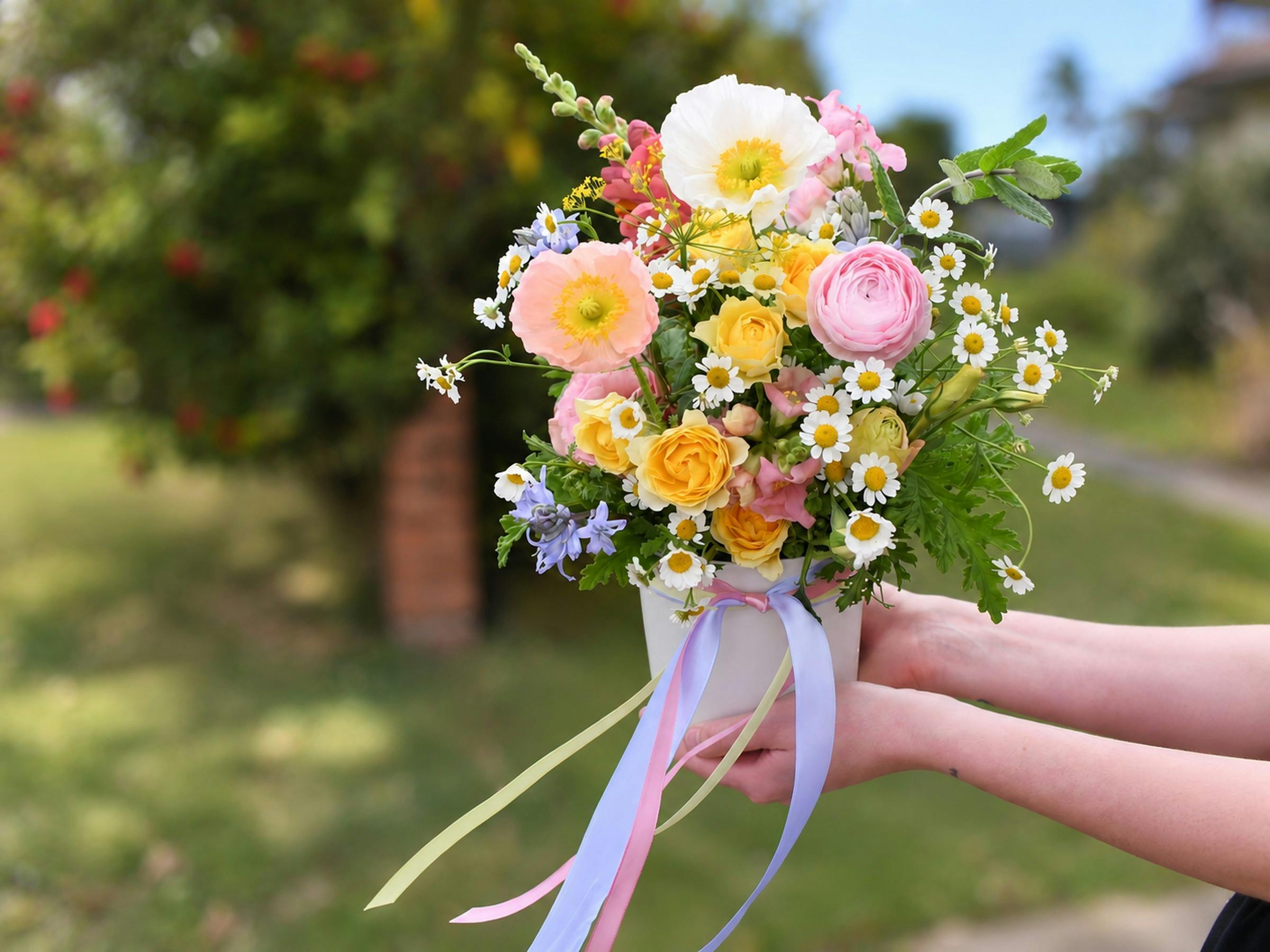 Colourful floral arrangement featuring pink and yellow roses, white daisies, pastel flowers and gree