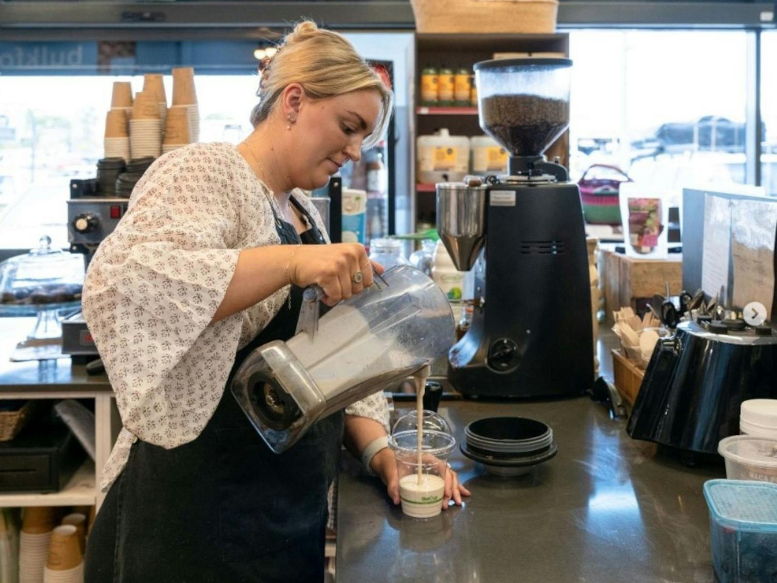 A lady wearing an apron and pouring a smoothy from a blender into a cup