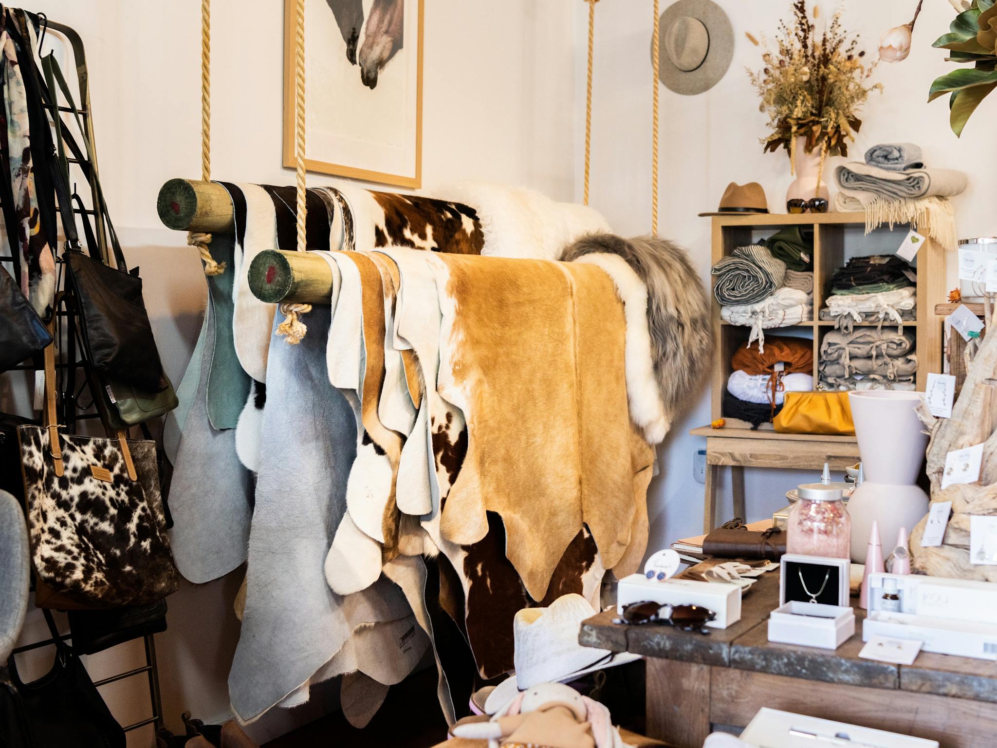 Cowhides and sheepskins hanging on timber poles suspended by rope, a cupboard of bed and table linen