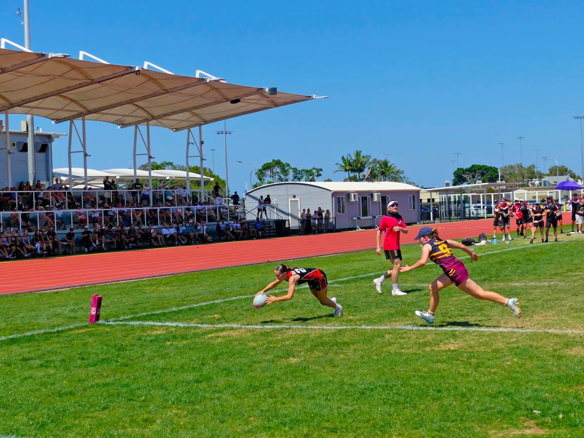 A young female touch player dives to score a try and elude an opposition player