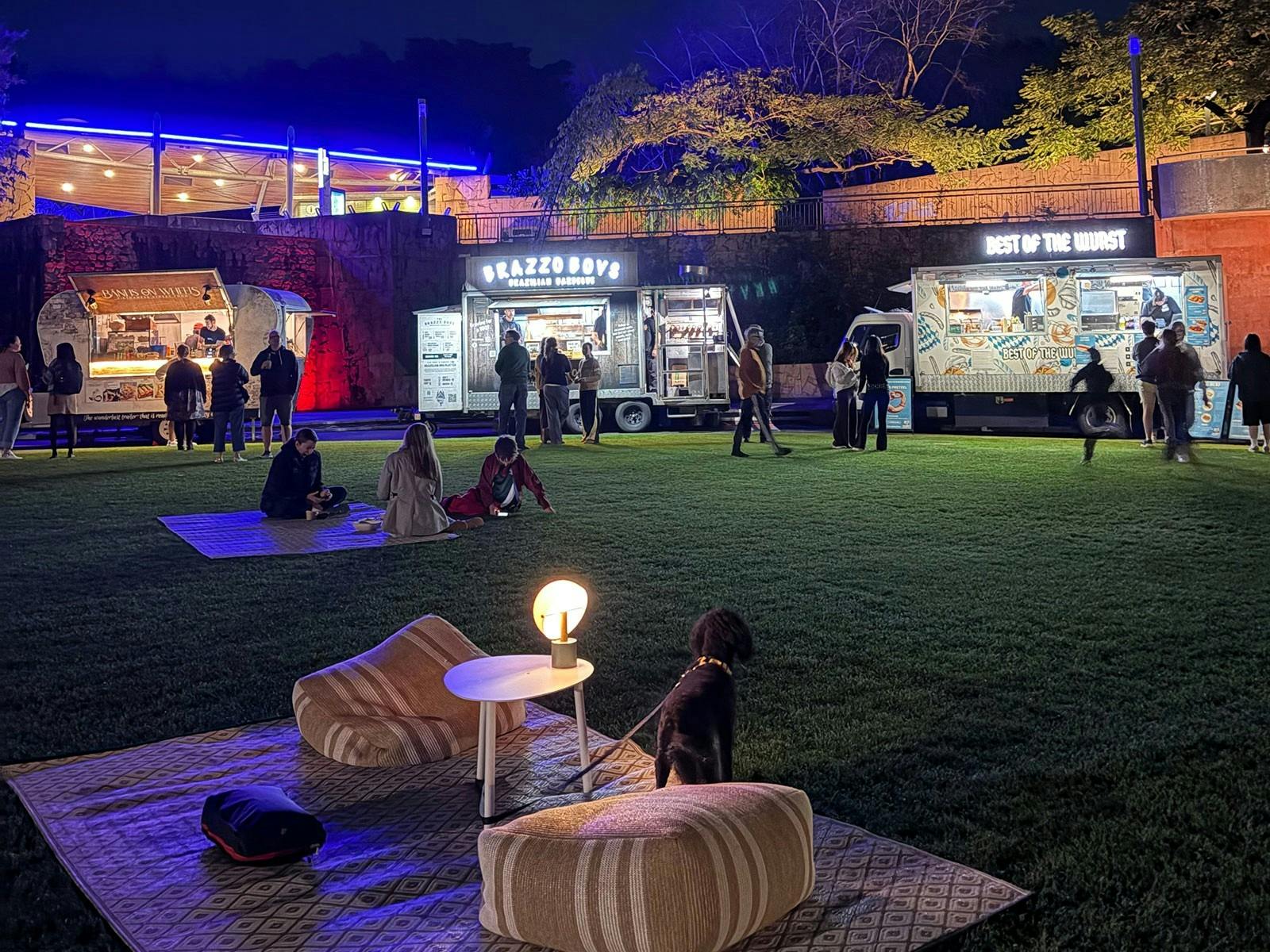 Lawn area outdoors at night set with picnic rugs and food trucks on the perimeter of the lawn