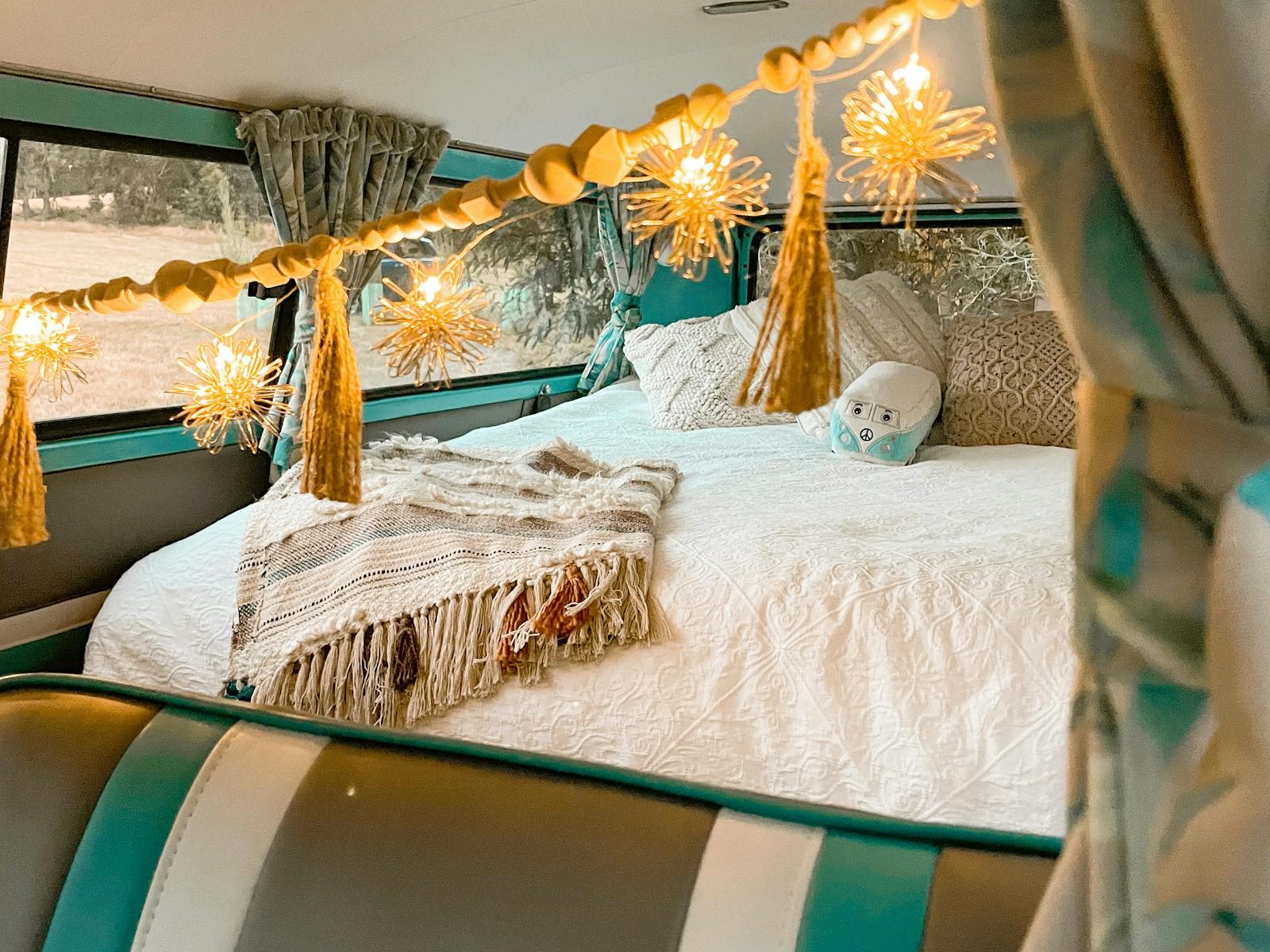Interior of kombi showing the bed with white linen, cushions, throws and fairy lights.
