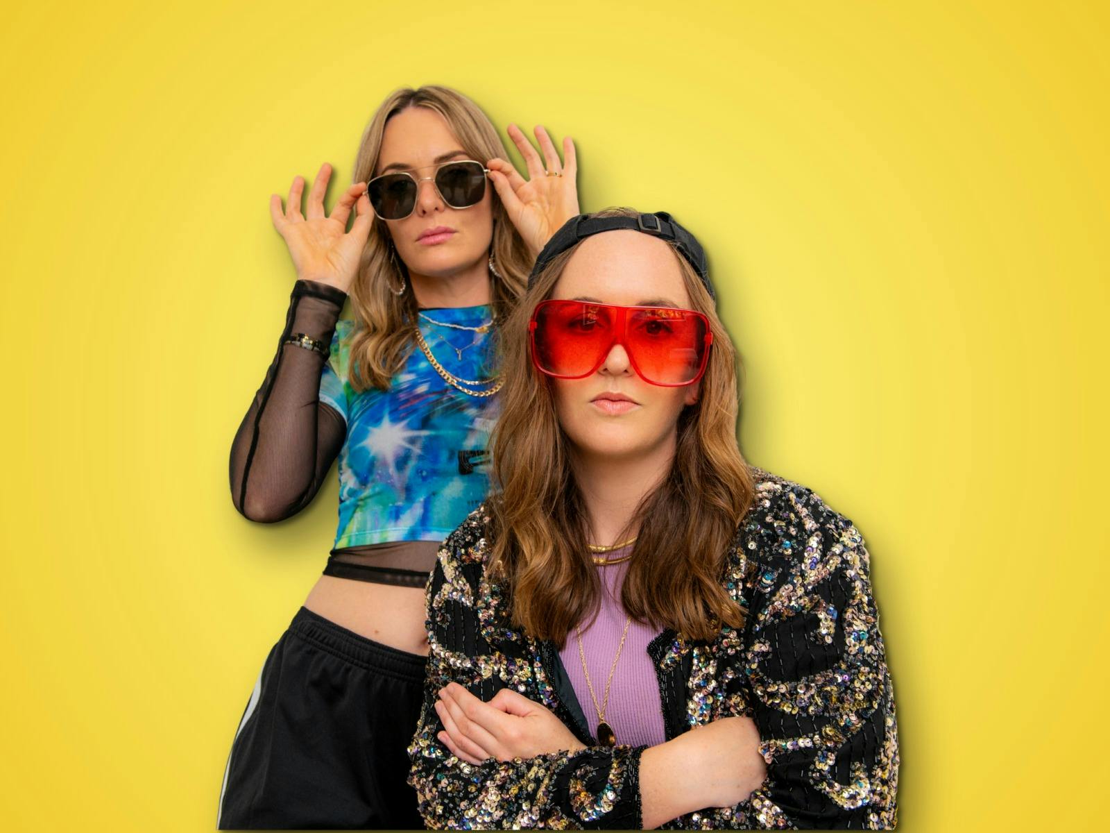 Musical comedy duo Emma and Maddie pose menacingly in sparkly outfits