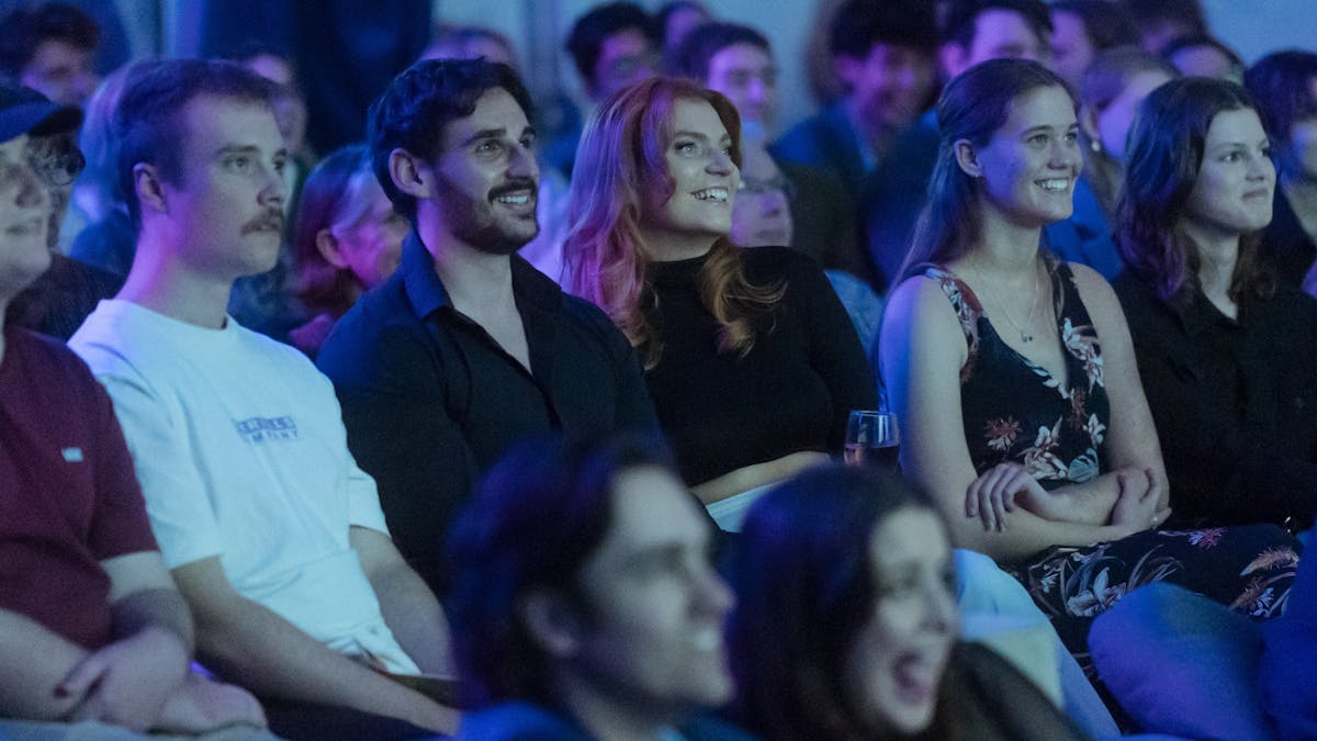 A group of people are seated in an audience, smiling and engaged.