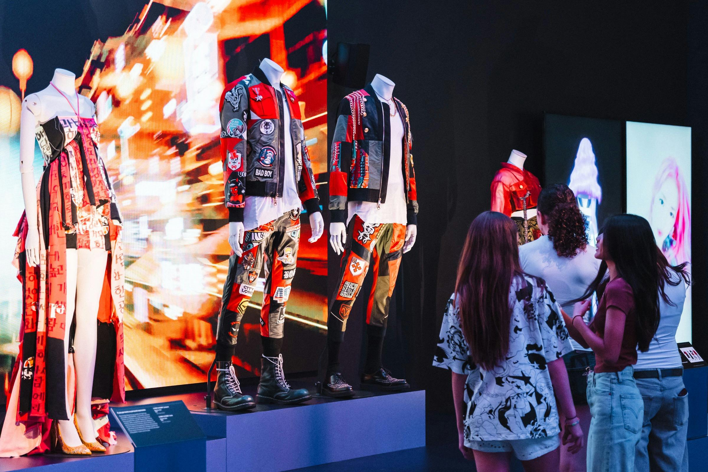 Korean fashion being displayed on mannequins in an exhibition and three young girls  looking at them