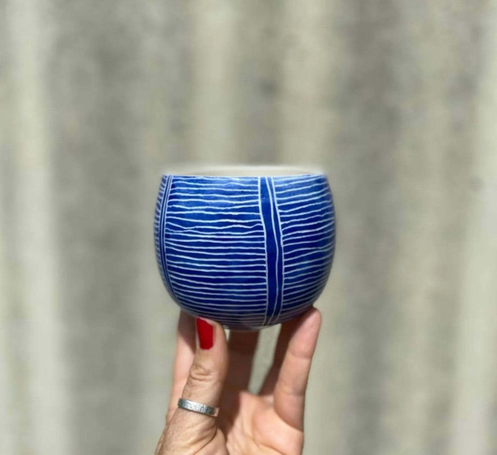 Small Blue and white striped ceramic mug being held up high