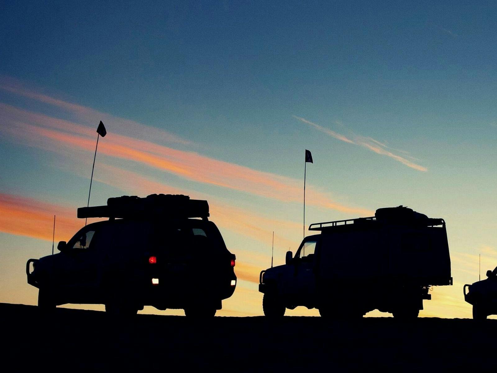 Silhouette of 4x4 cars against an orange and blue sky at sunset.