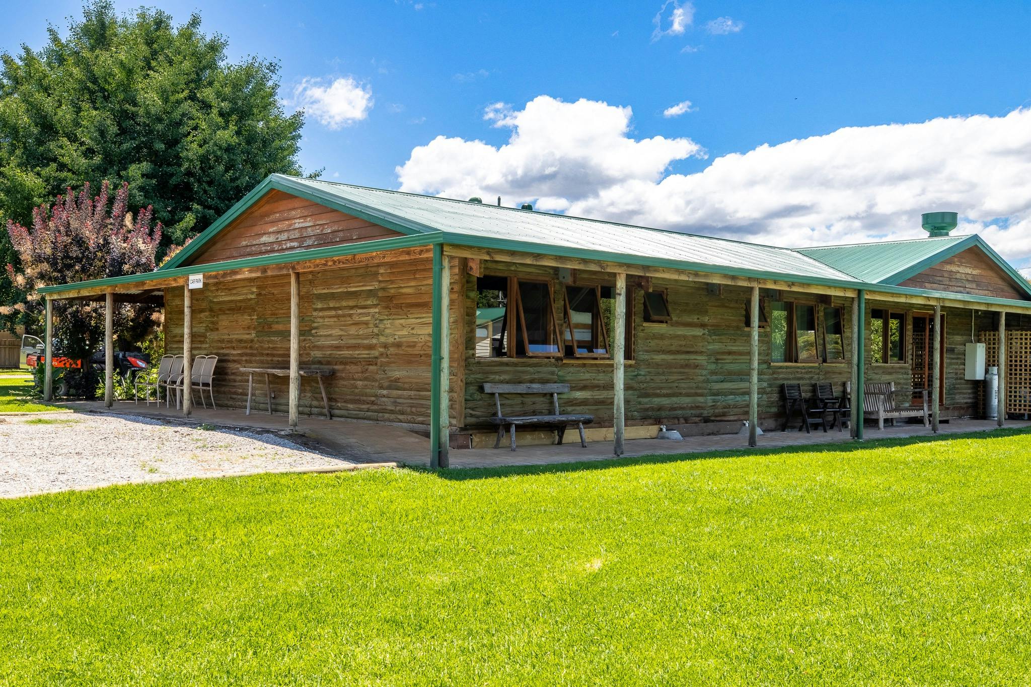exterior of a wooden cabin with wooden chairs and benches outside surrounded by green grass