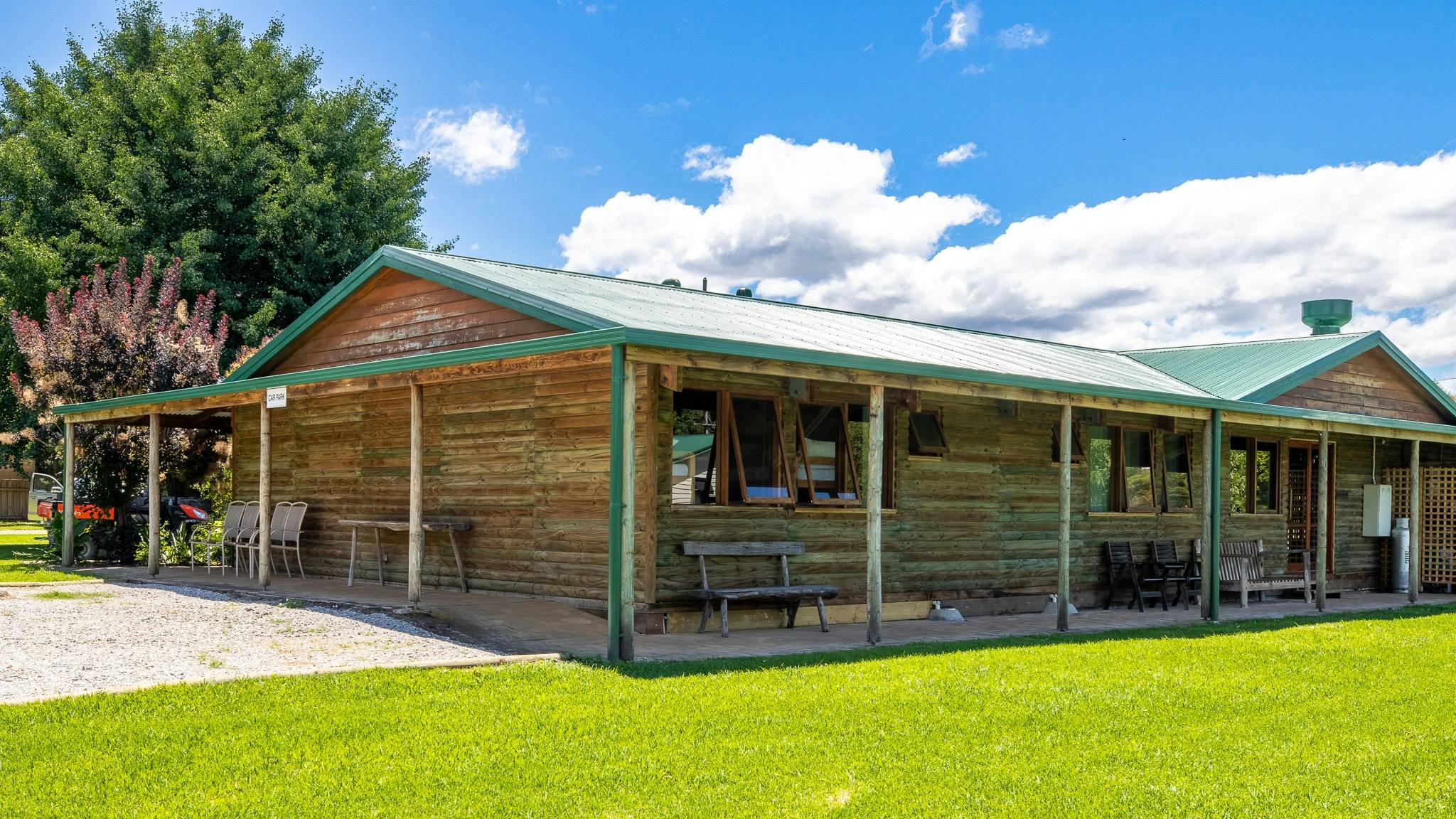 exterior of a wooden cabin with wooden chairs and benches outside surrounded by green grass
