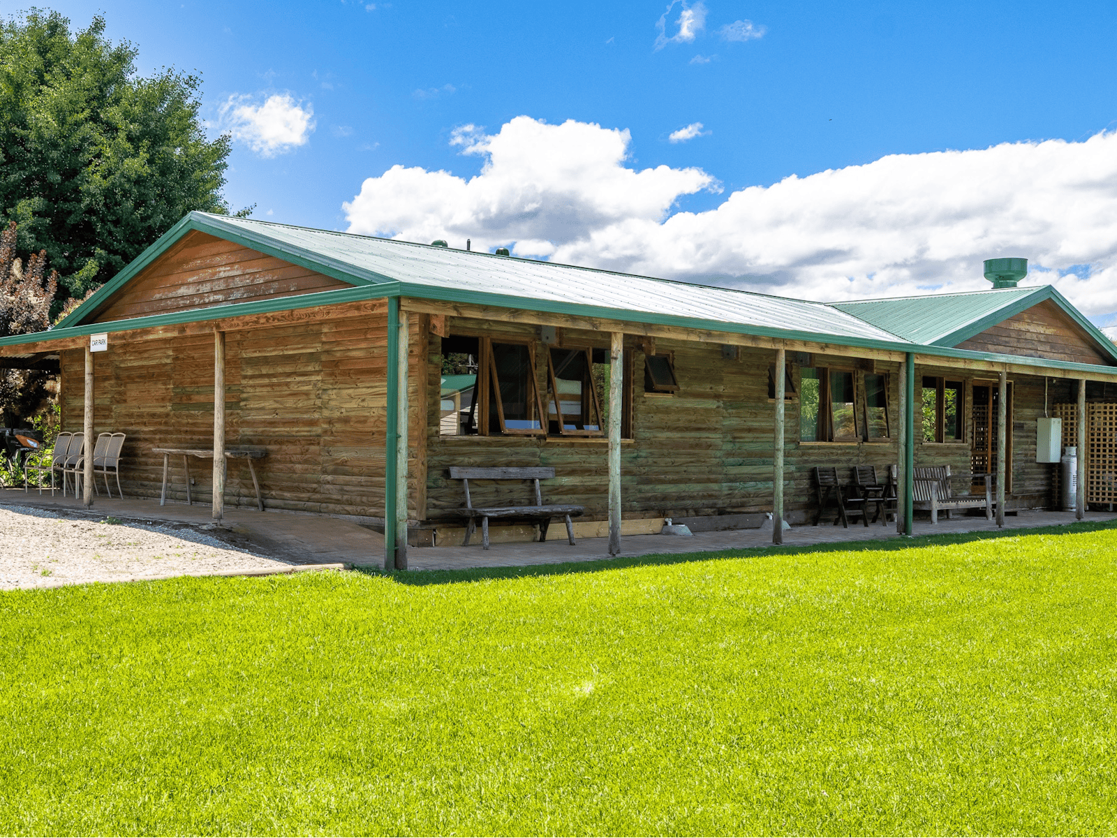 exterior of a wooden cabin with wooden chairs and benches outside surrounded by green grass