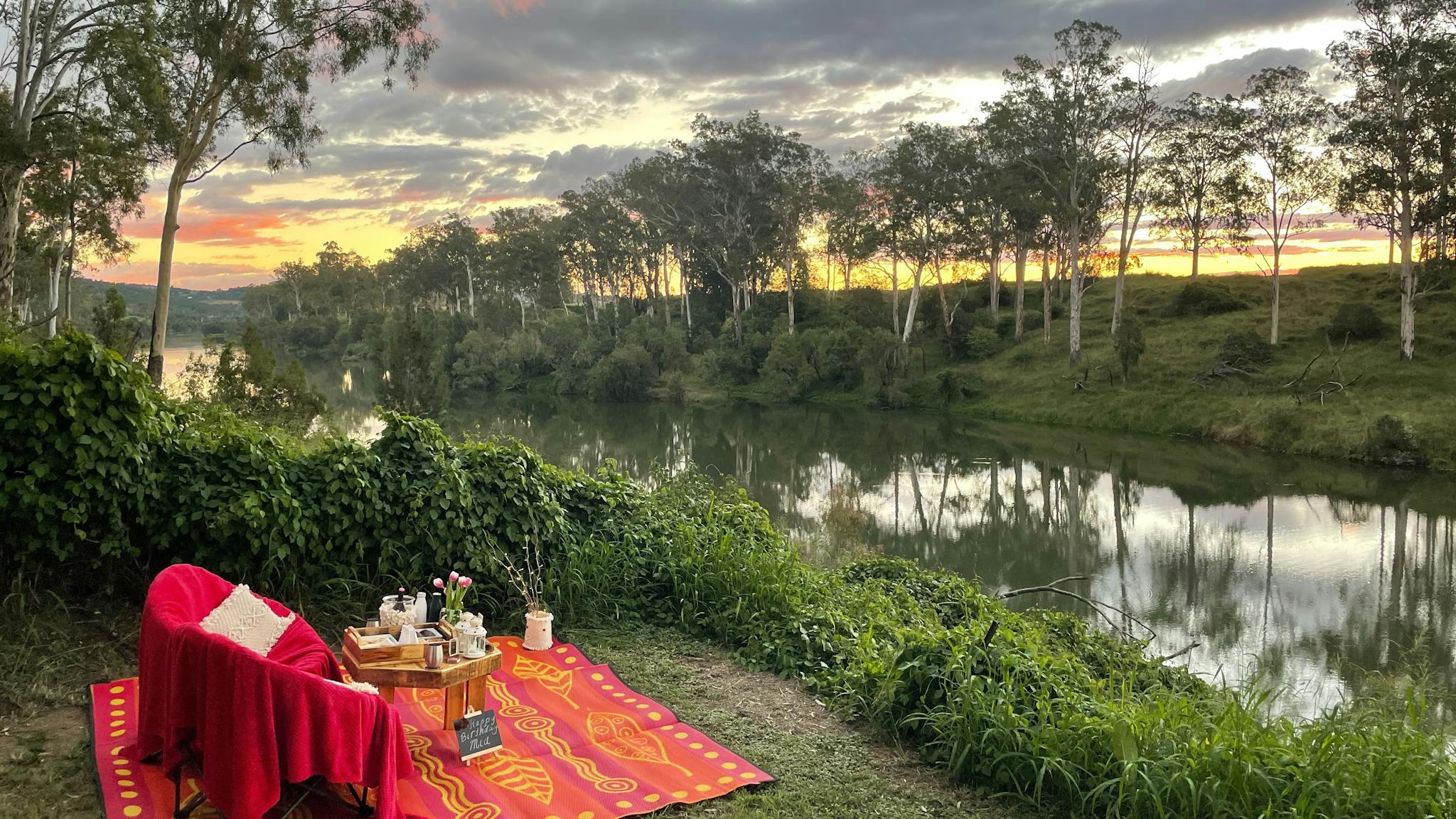 Picnic spot with rug, chairs and picnic with the sun setting over the river