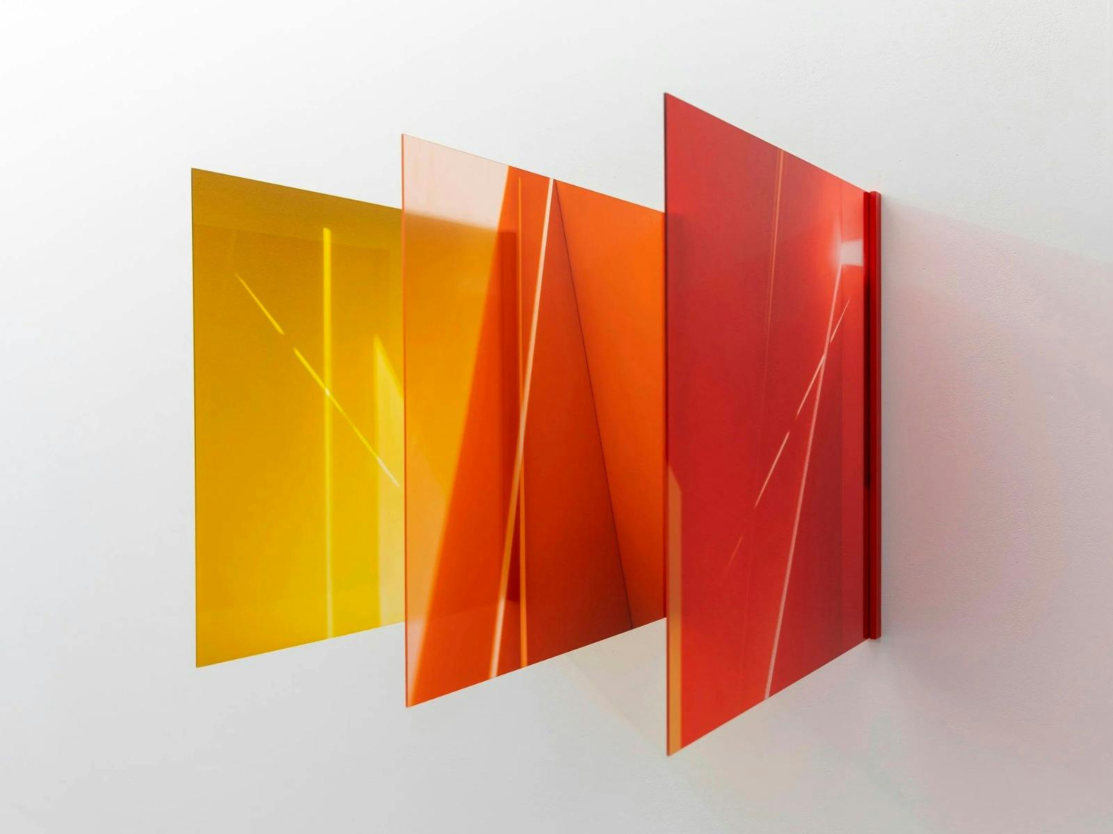 Three glass panels transitioning from yellow, orange and red jut out of a white wall