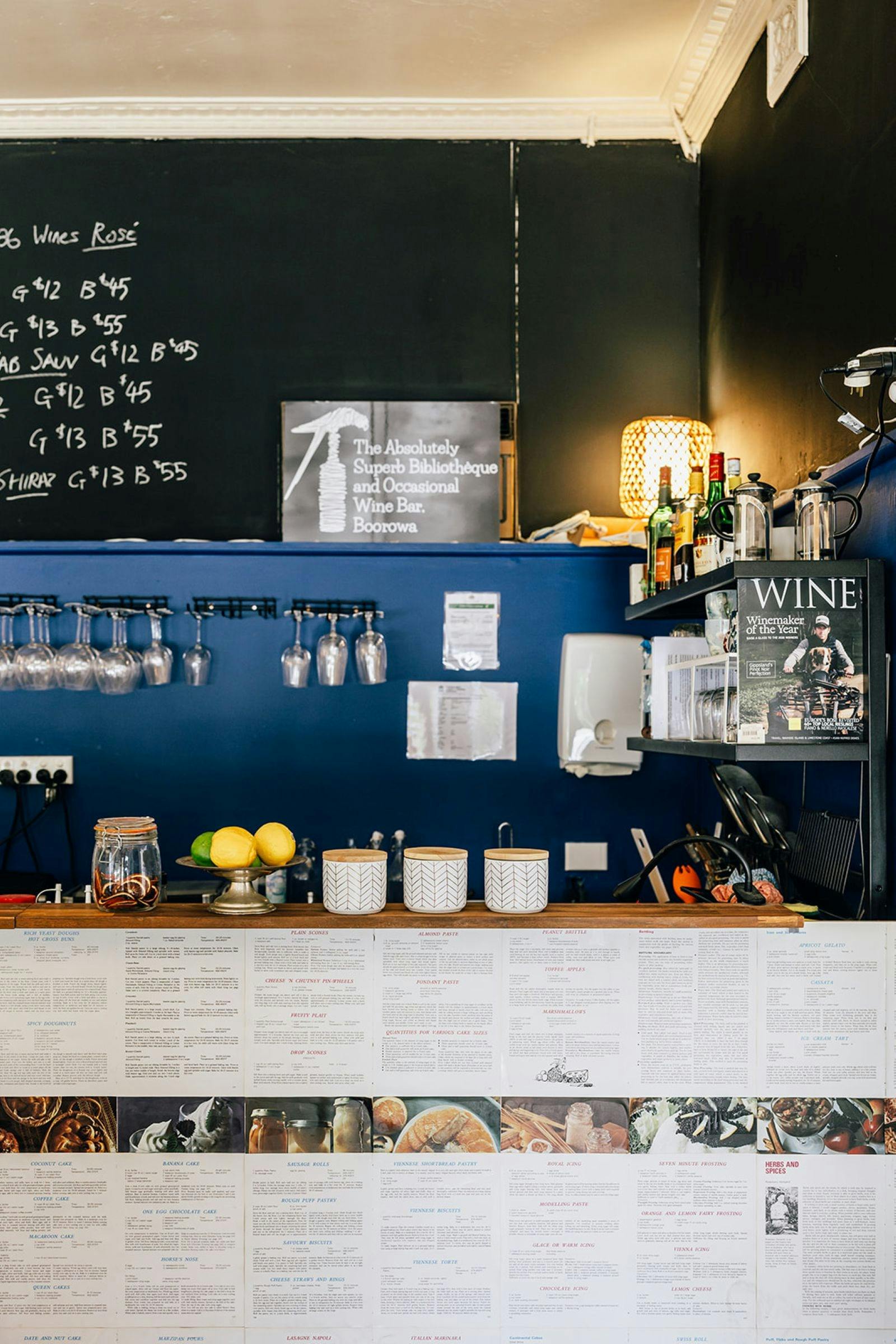 Wine bar with glasses hanging, lemons on counter, books and lamp making it dark and cosy.