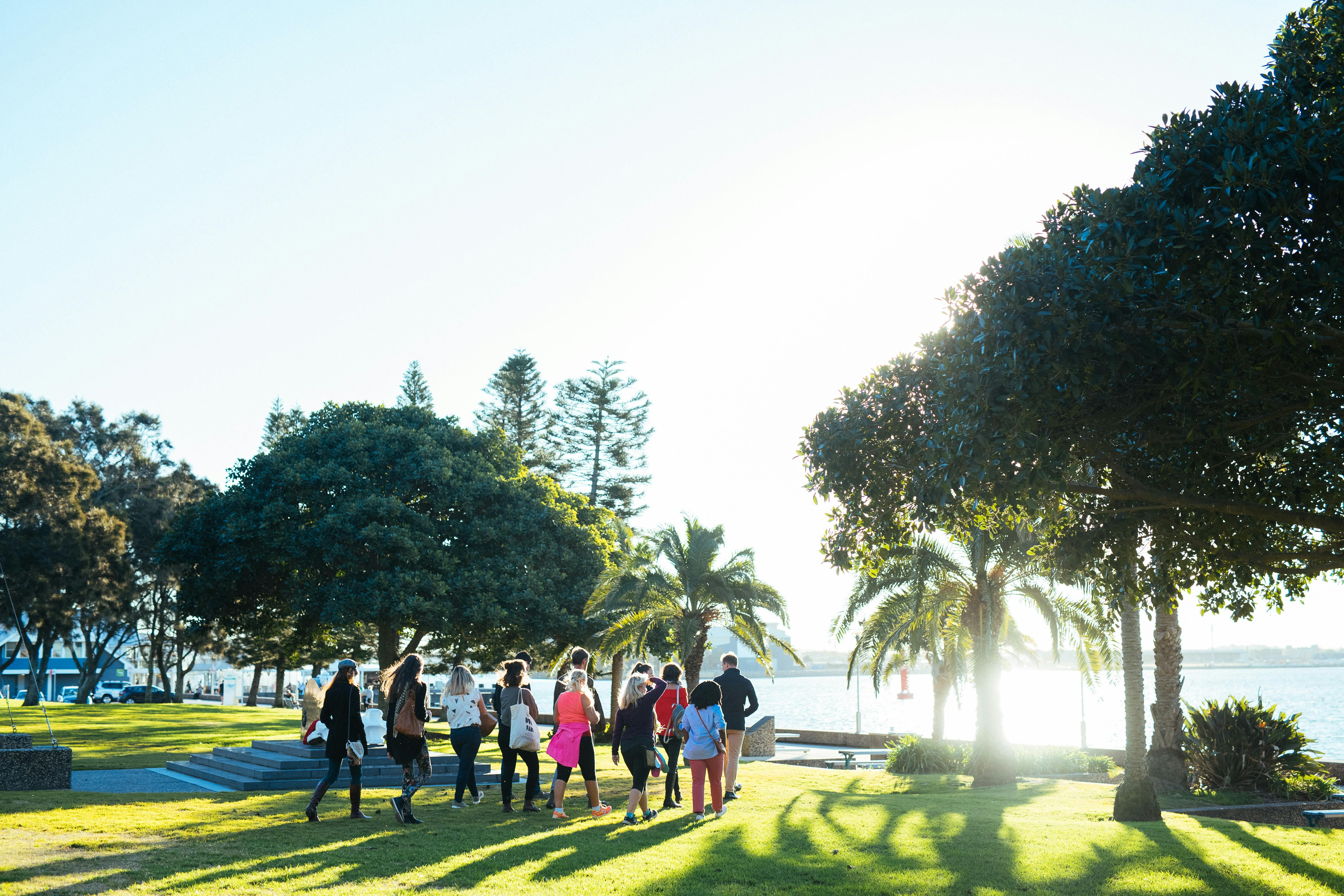 A small group walking through parkland next to the Hunter River on a Newcastle Afoot walking tour