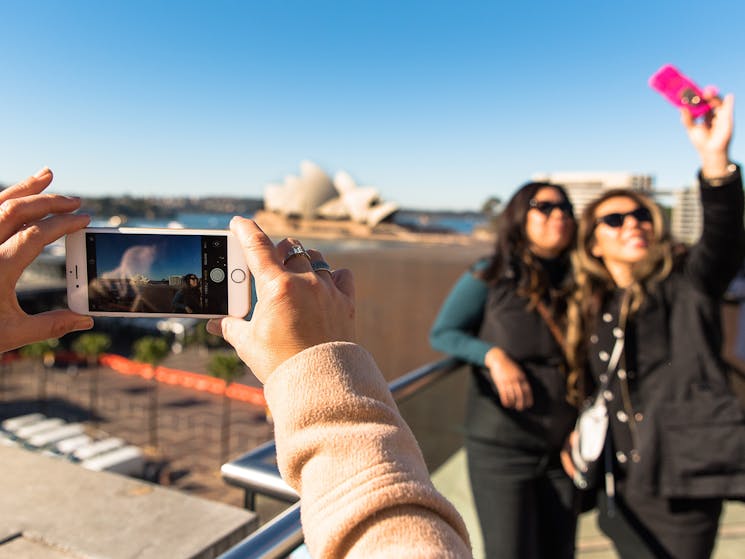 Smartphone photographer of the Opera House with two nearby woman taking a selfie