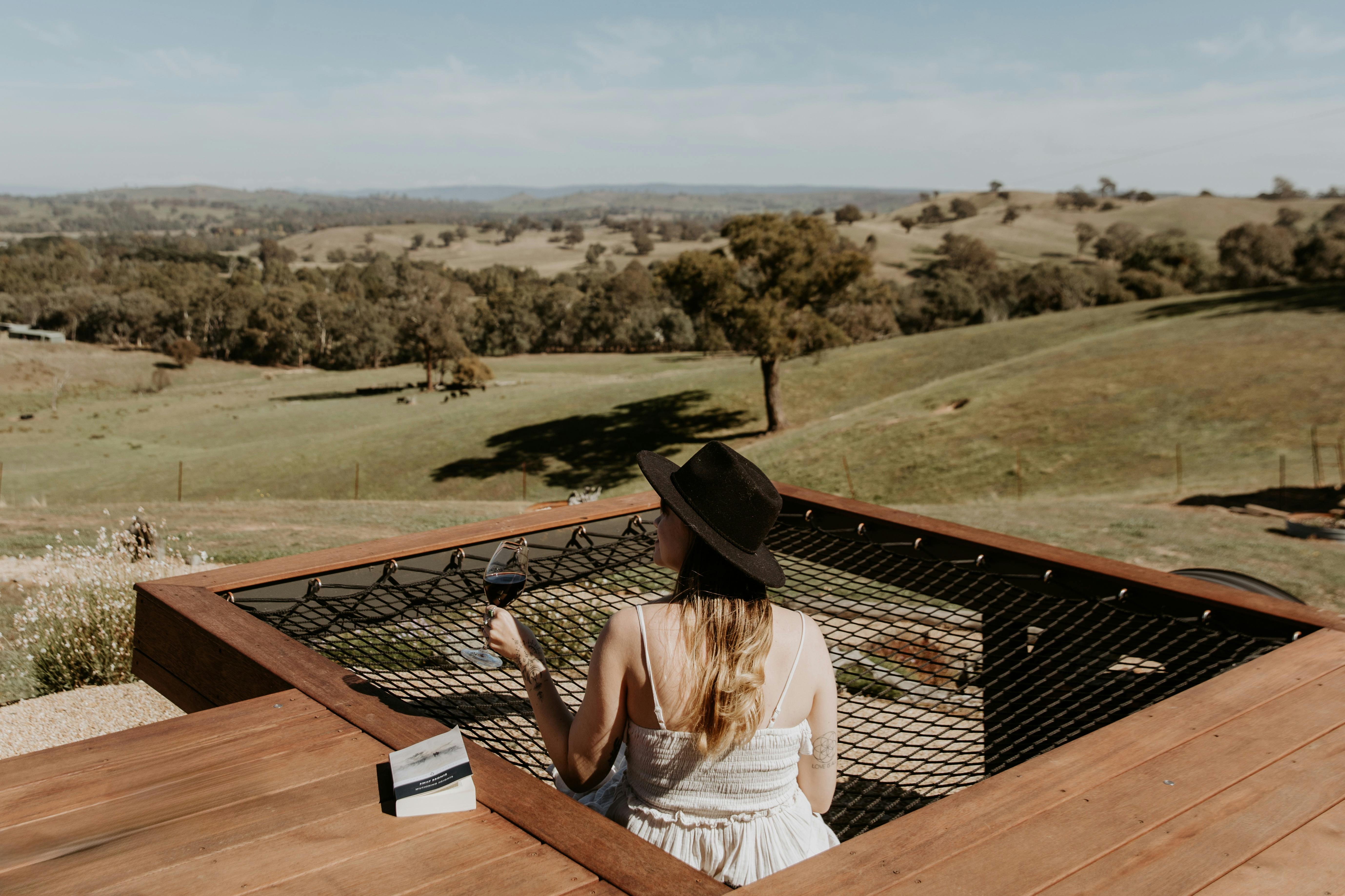 Woman admiring view in large net hammock in decking overlooking valley with rolling hills