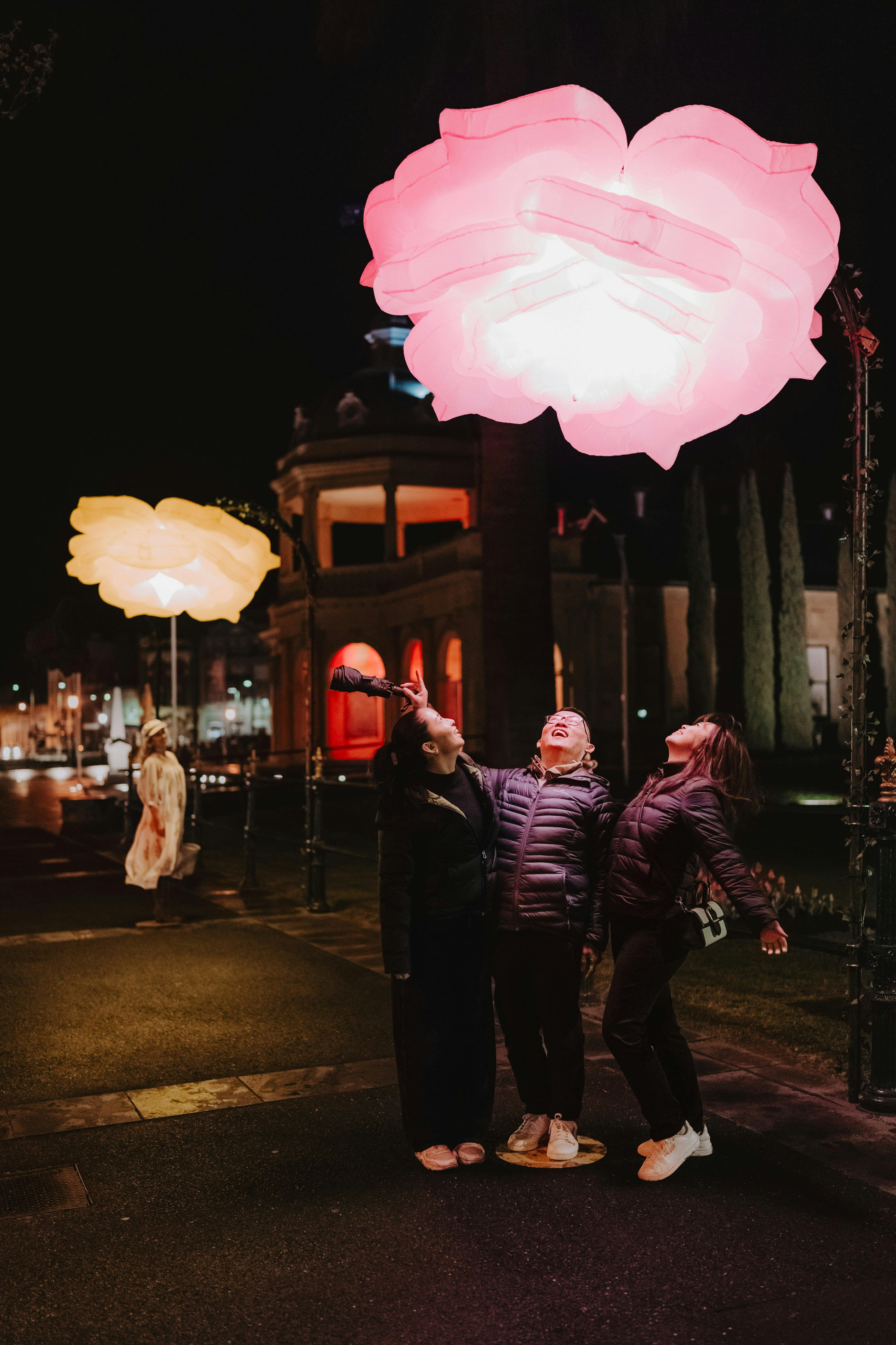 A group of 3 family members standing together under a giant illuminated flower