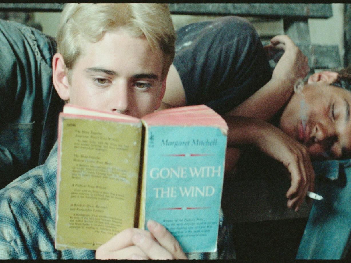 One male lying on couch sleeping, another sitting in front reading a book