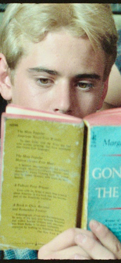 One male lying on couch sleeping, another sitting in front reading a book