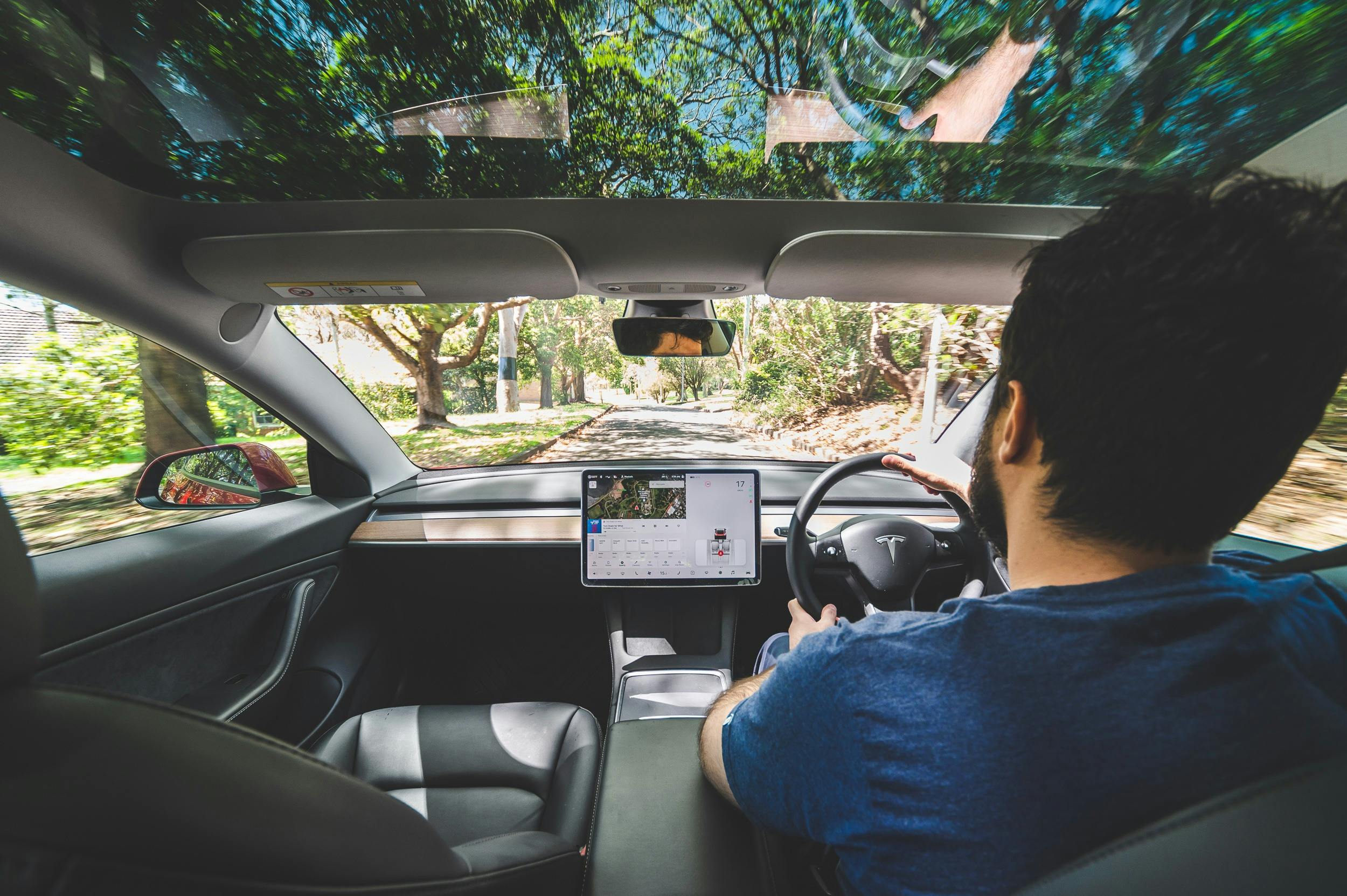 Image take from inside a Tesla from the backseat, view of a the driver from behind