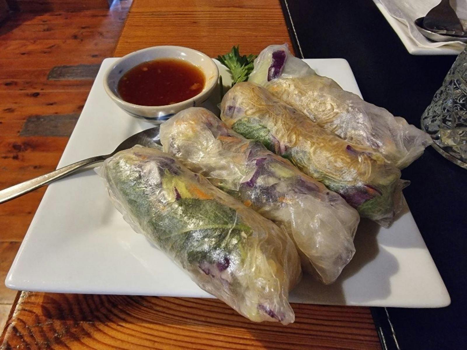 Three rice paper rolls on a square white plate with a dipping sauce on the side