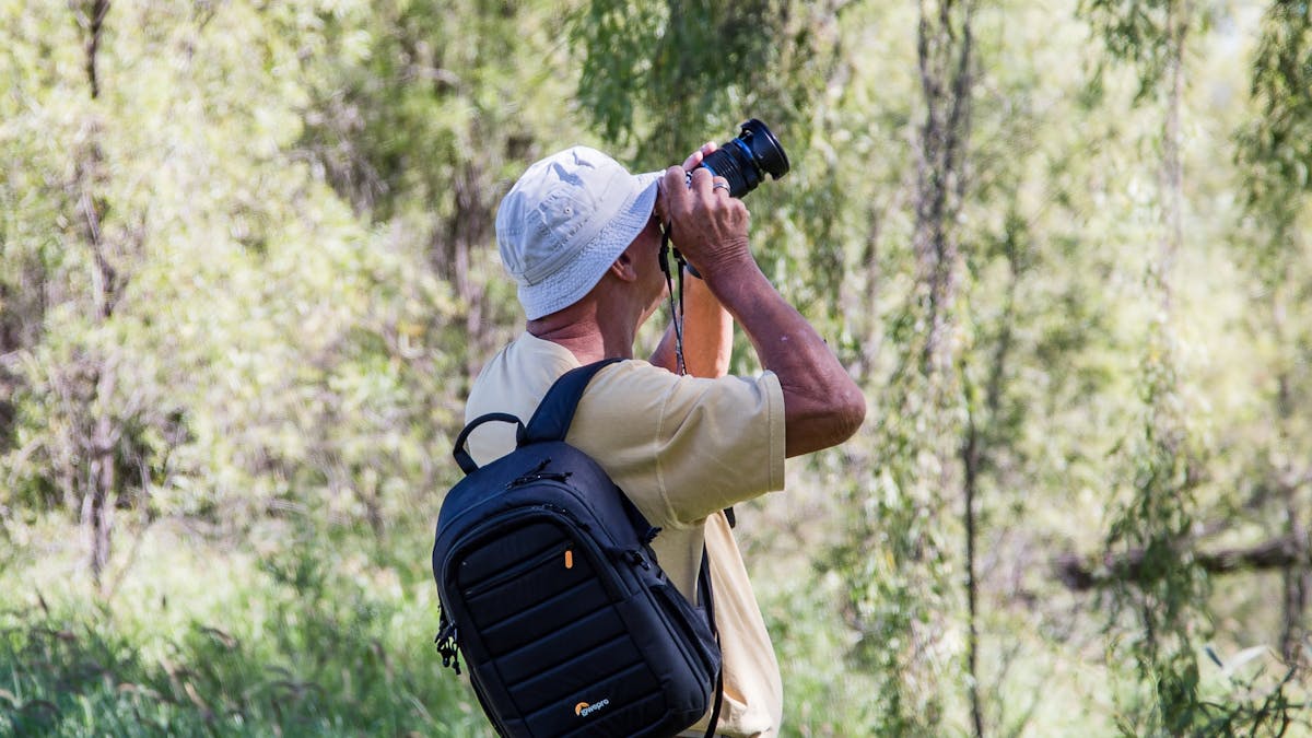 A man in a bucket hat pointing a camera upwards
