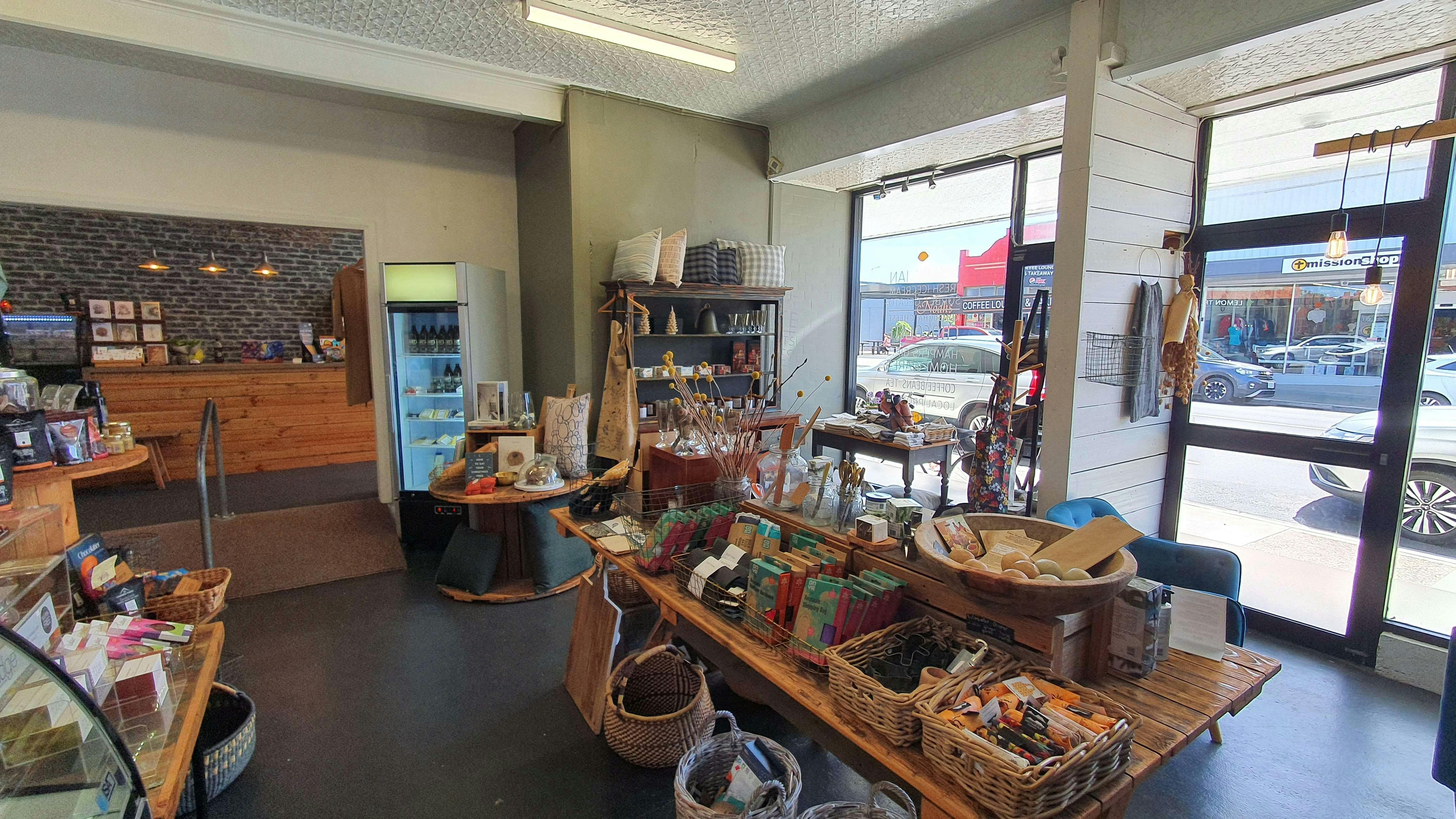 Interior of a shop, with white walls, a wooden table with a colourfil display, and windows